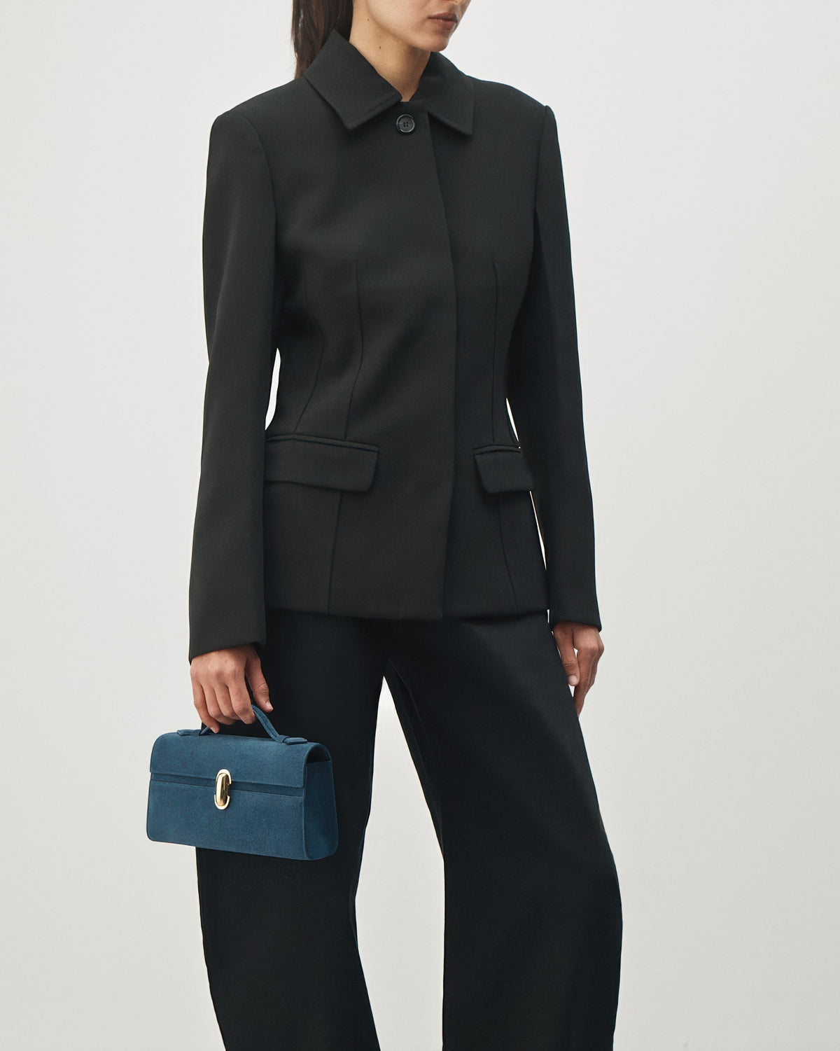 on-model view of a baltic blue suede top handle bag with a gold clasp on a white background 
