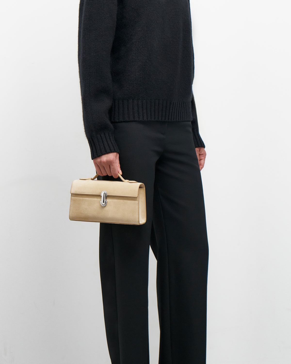 on model view of a flax beige suede bag with a silver clasp on a white background