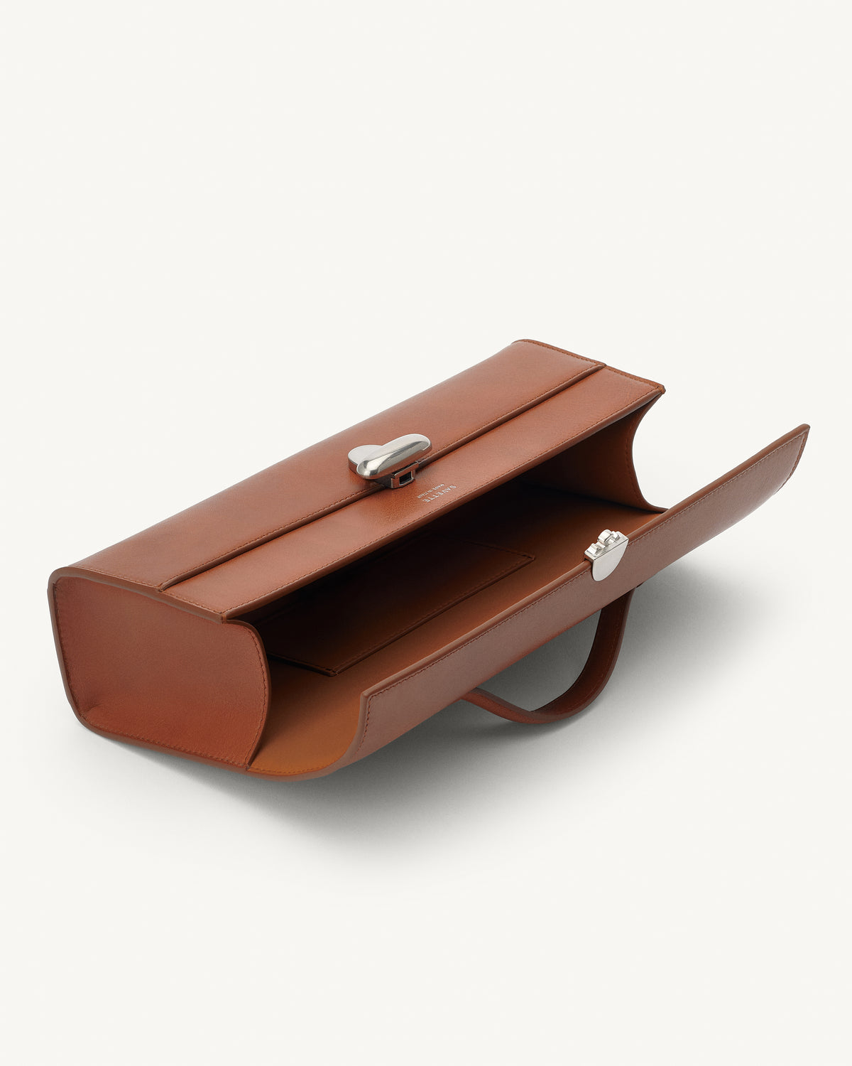 interior view of a cognac brown leather top handle bag with a silver clasp on a white background 