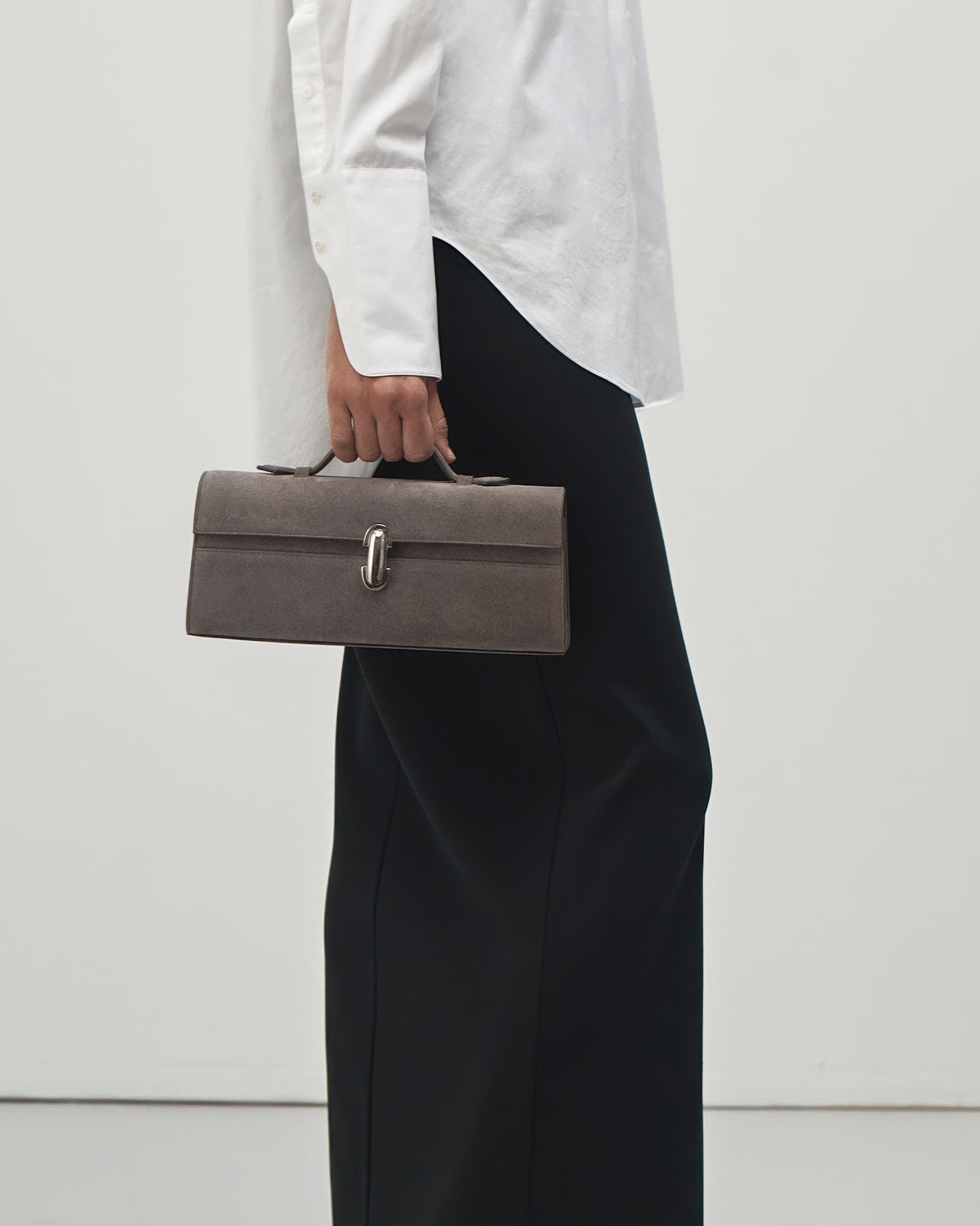 on-model view of a smoke grey suede handbag with a silver clasp on a white background 