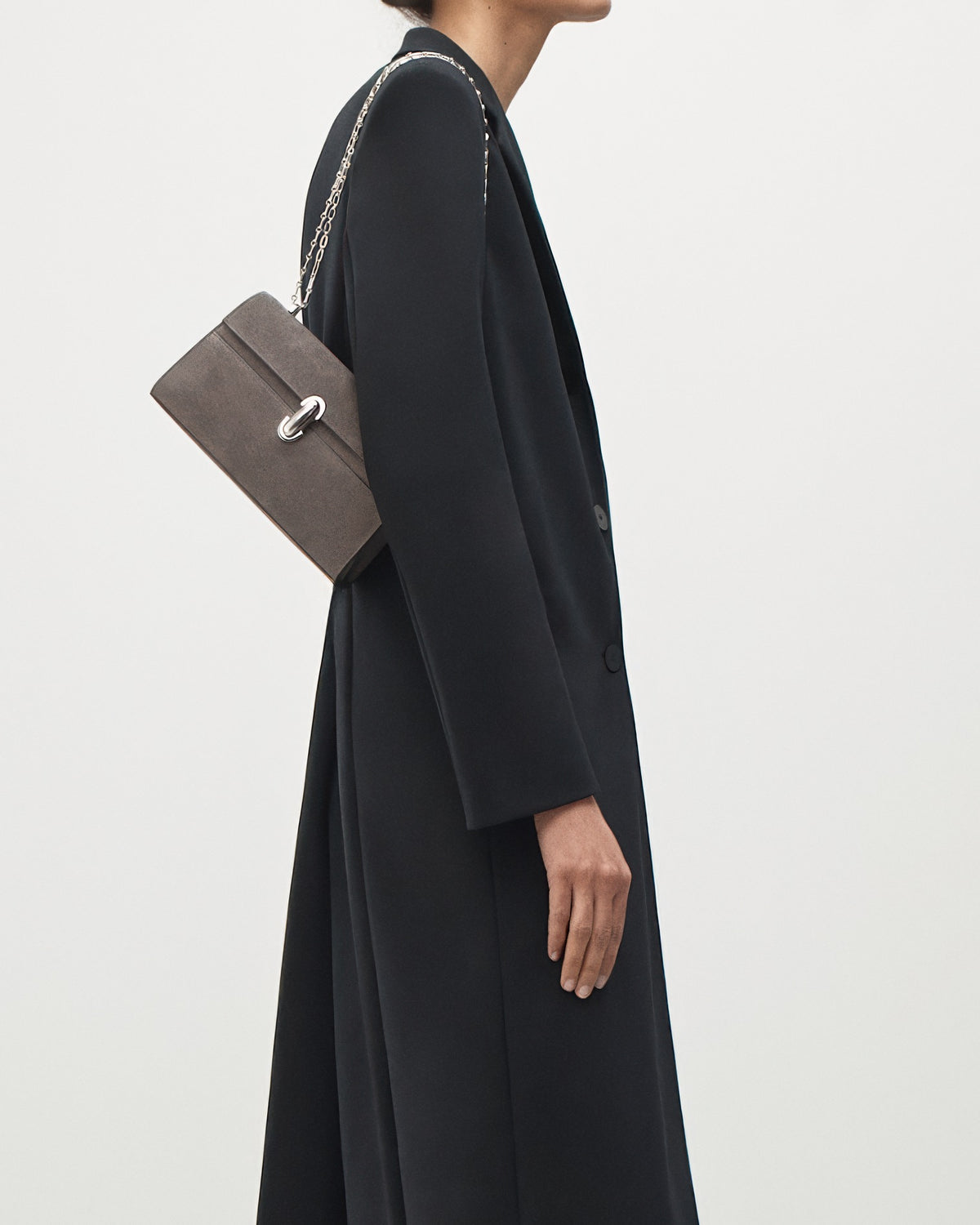 on-model view of a smoke grey suede bag with a silver chain and silver clasp on a white background 