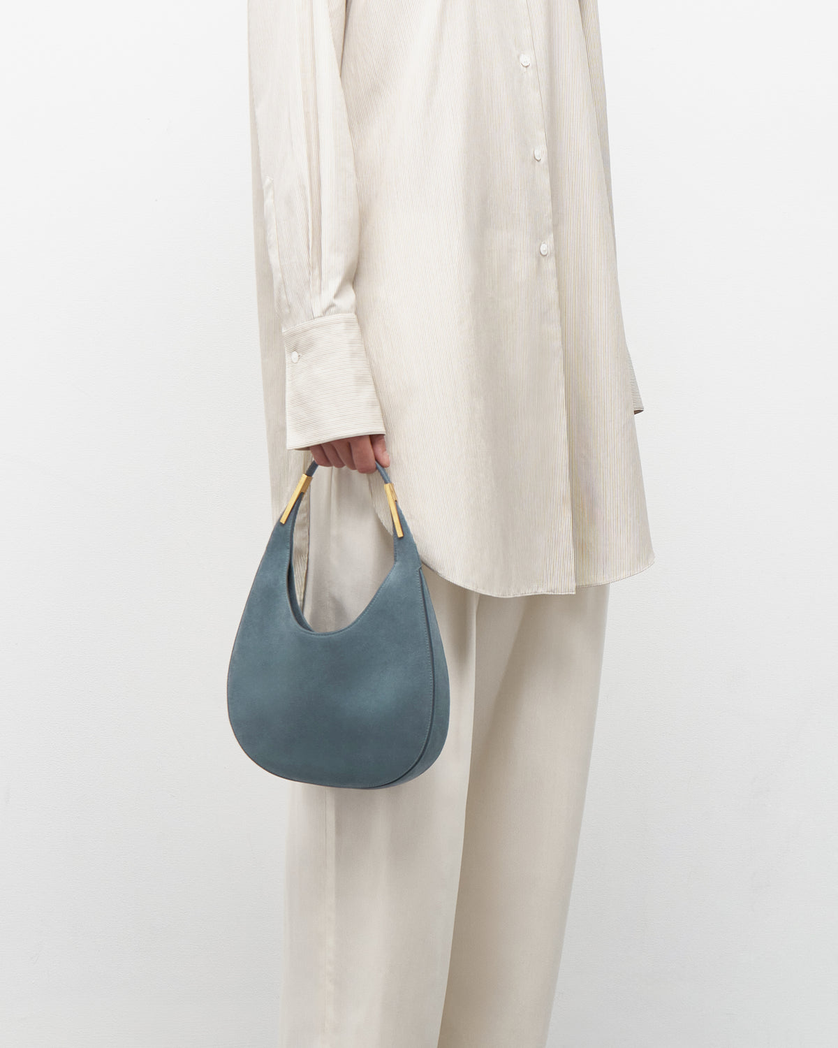 on model view of a denim blue suede bag with gold hardware on a white background