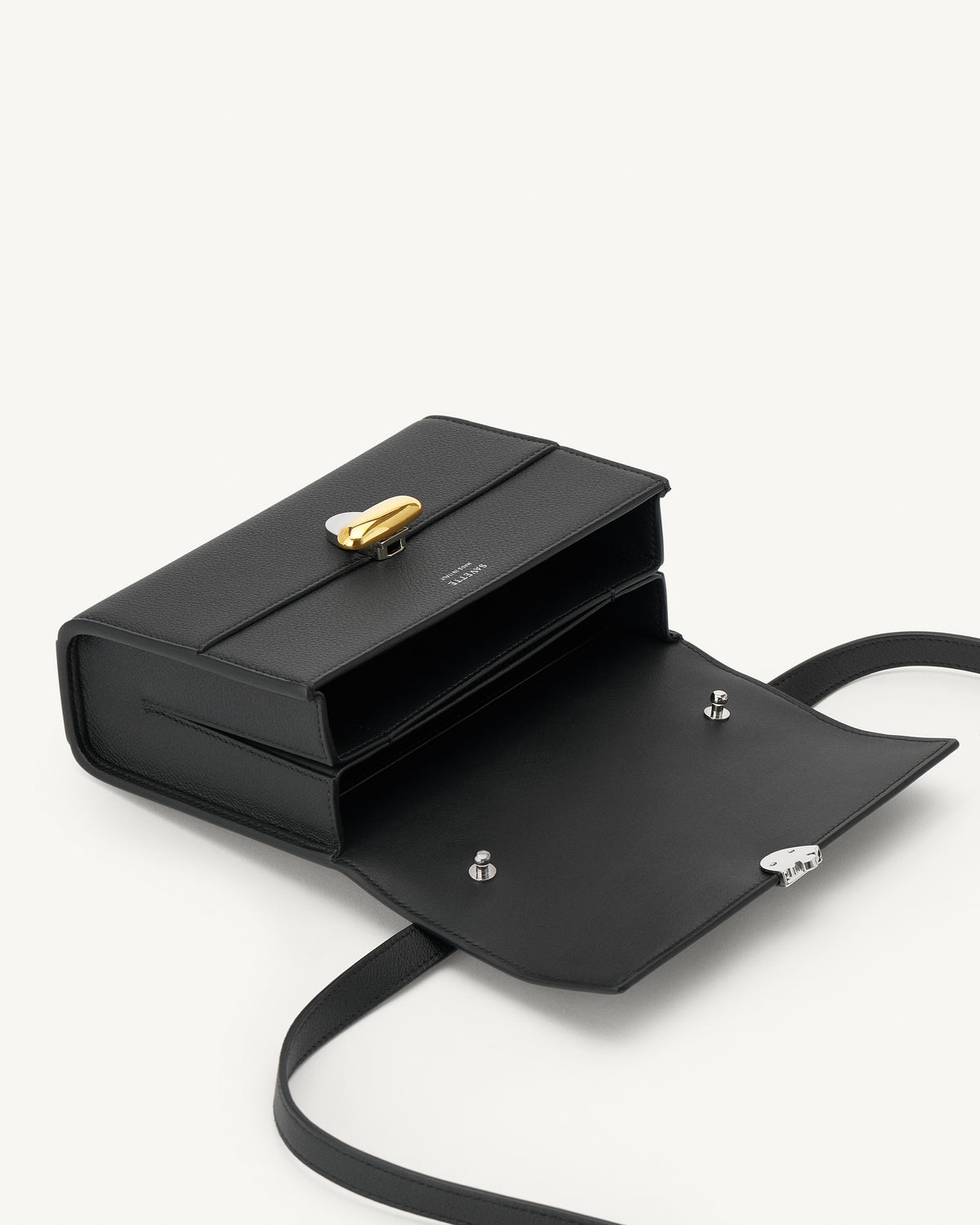 interior view of a black leather bag with a silver and gold clasp on a white background