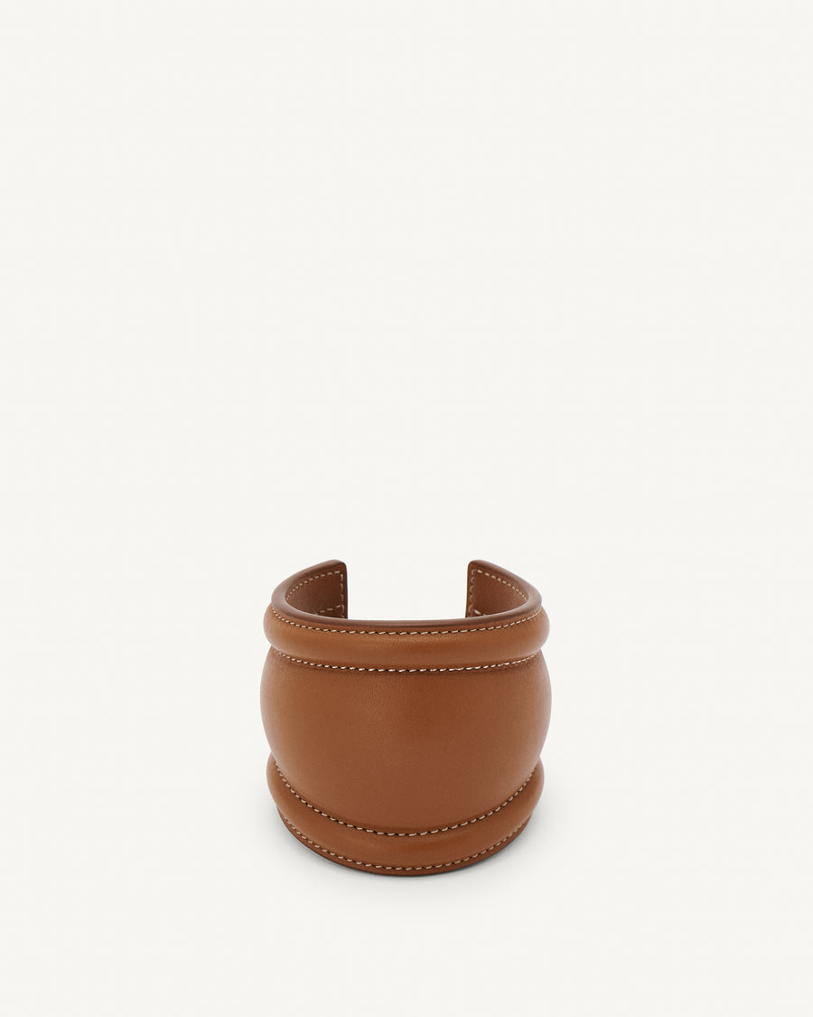 front view of a cognac brown leather cuff with white stitching on a white background 