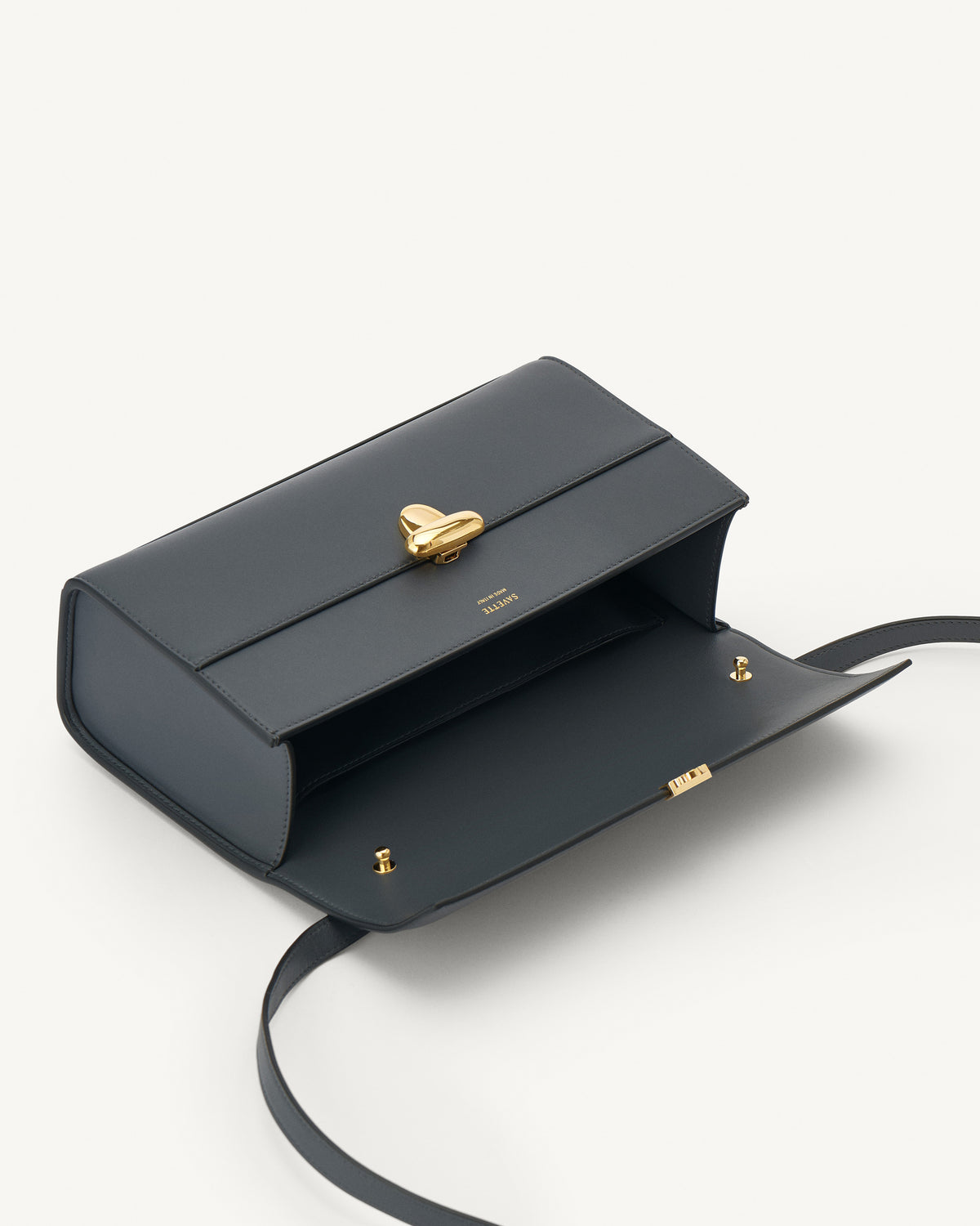 interior view of a storm blue leather bag with a gold clasp on a white background
