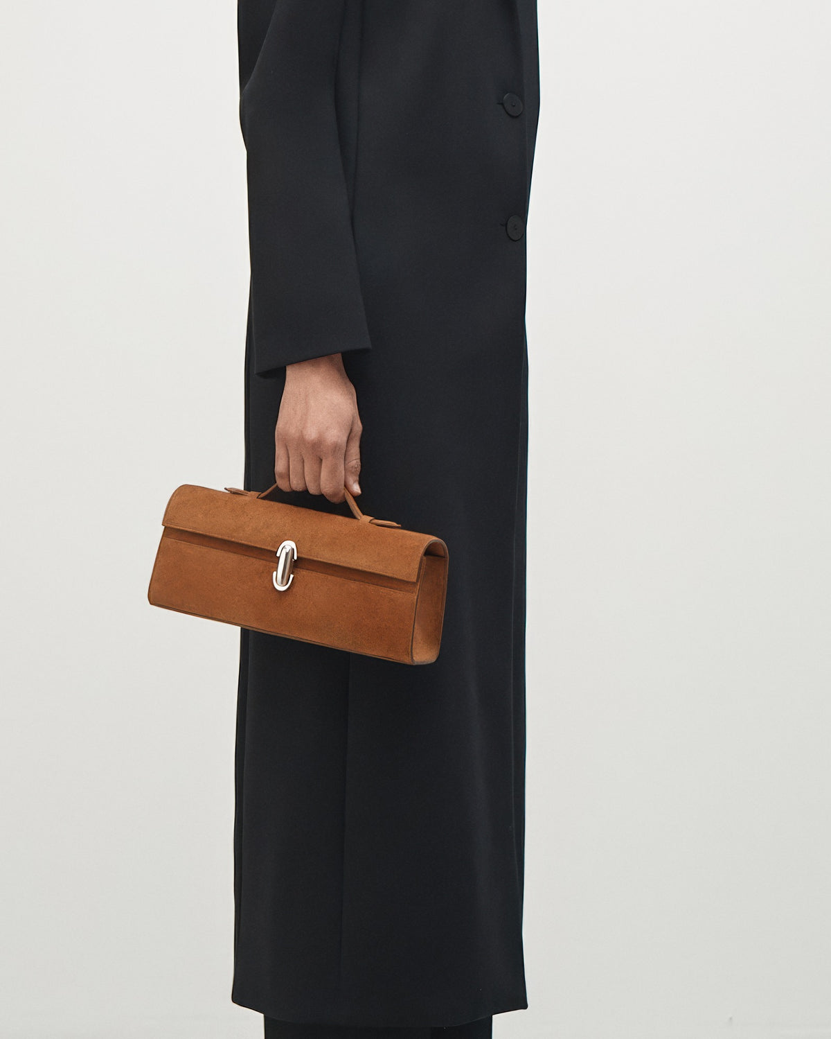 on-model view of a cognac brown suede top handle bag with a silver clasp on a white background 