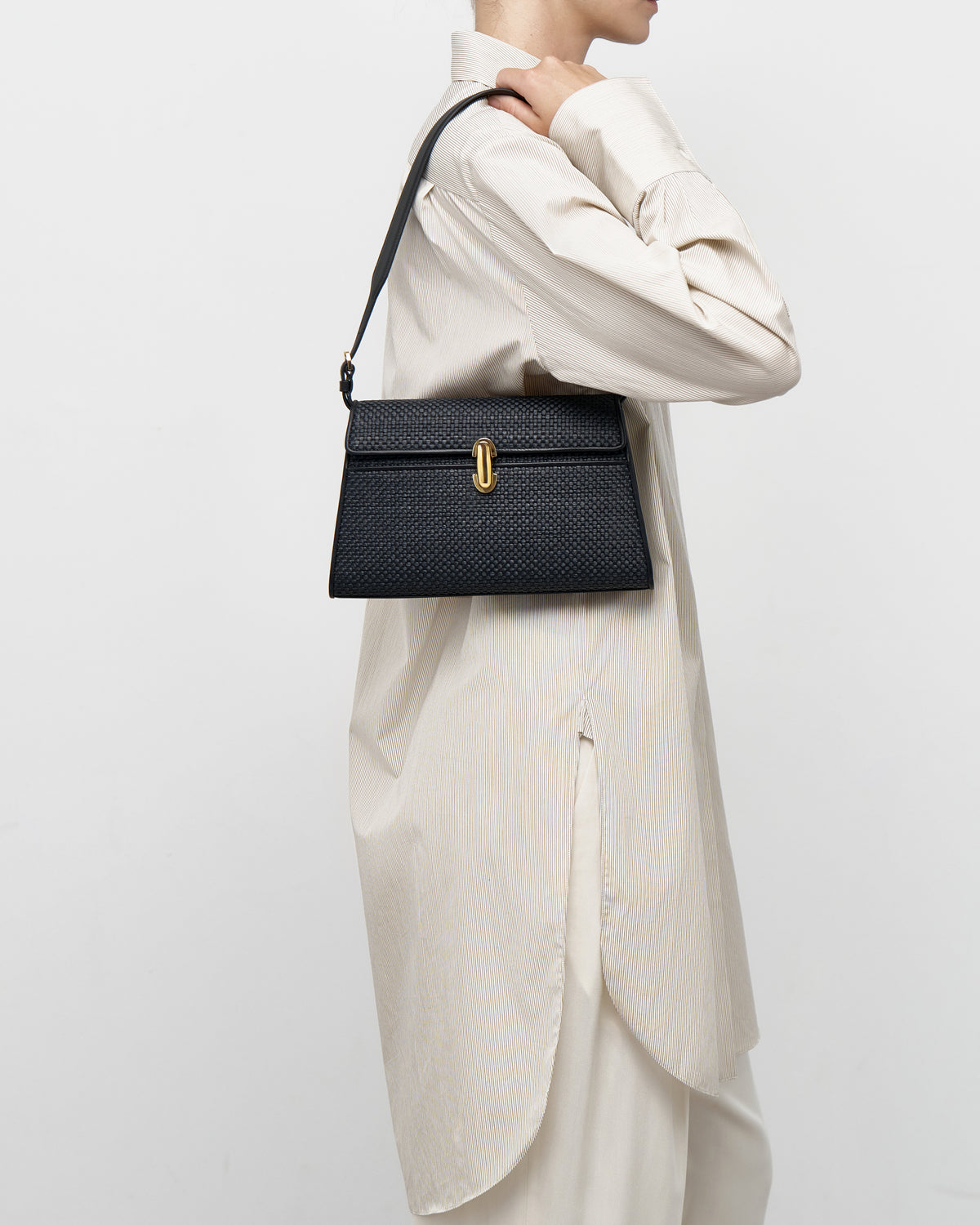 on model view of a black raffia bag with a gold clasp on a white background