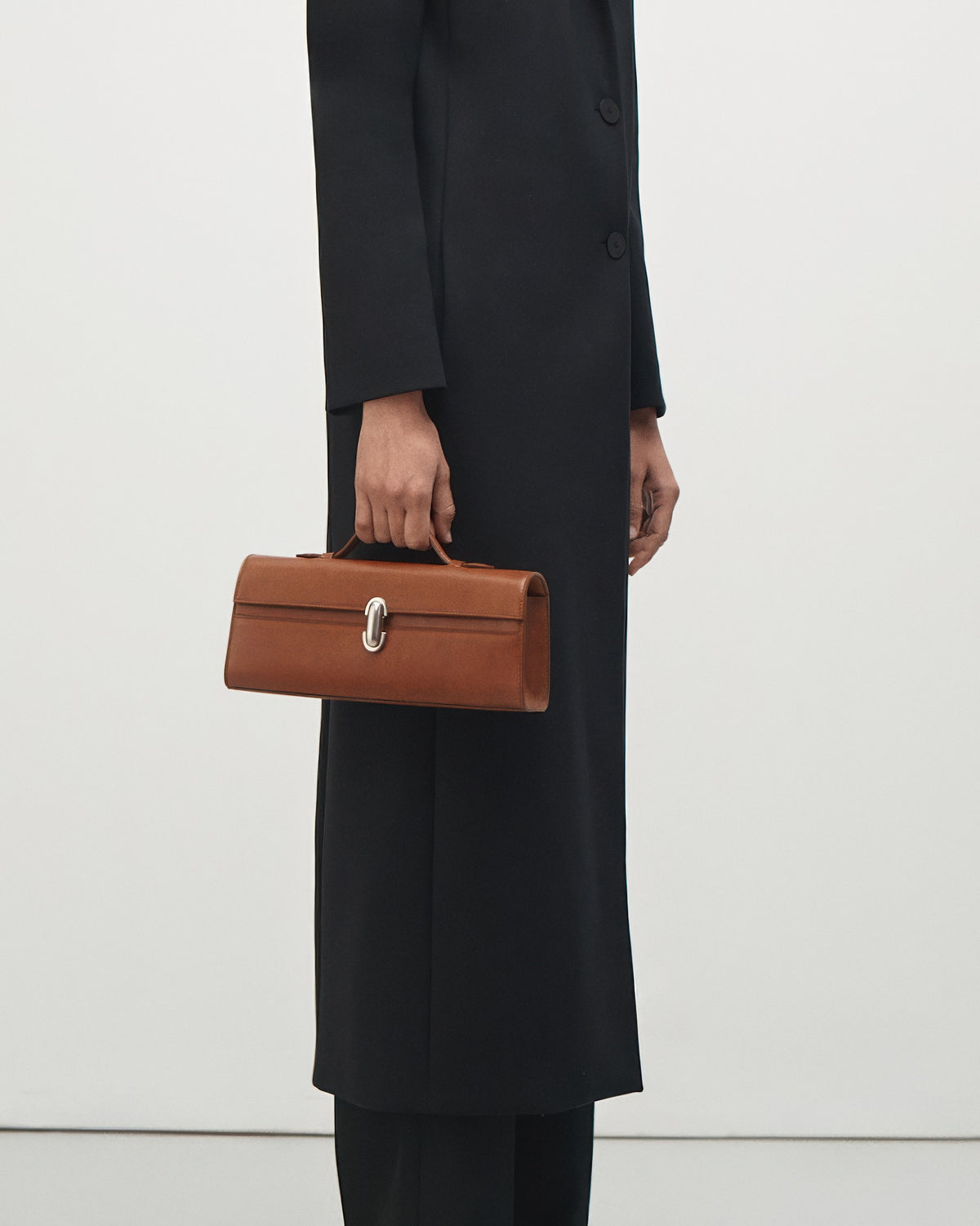 on model view of a cognac brown leather top handle bag with a silver clasp on a white background 