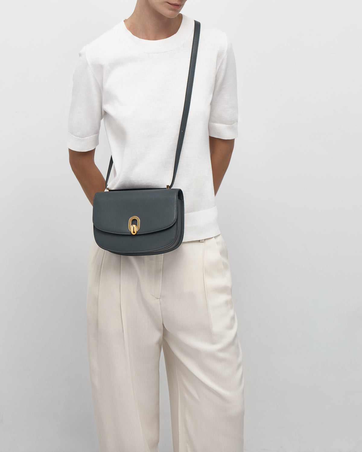 on model view of a storm blue leather bag with a gold clasp on a white background