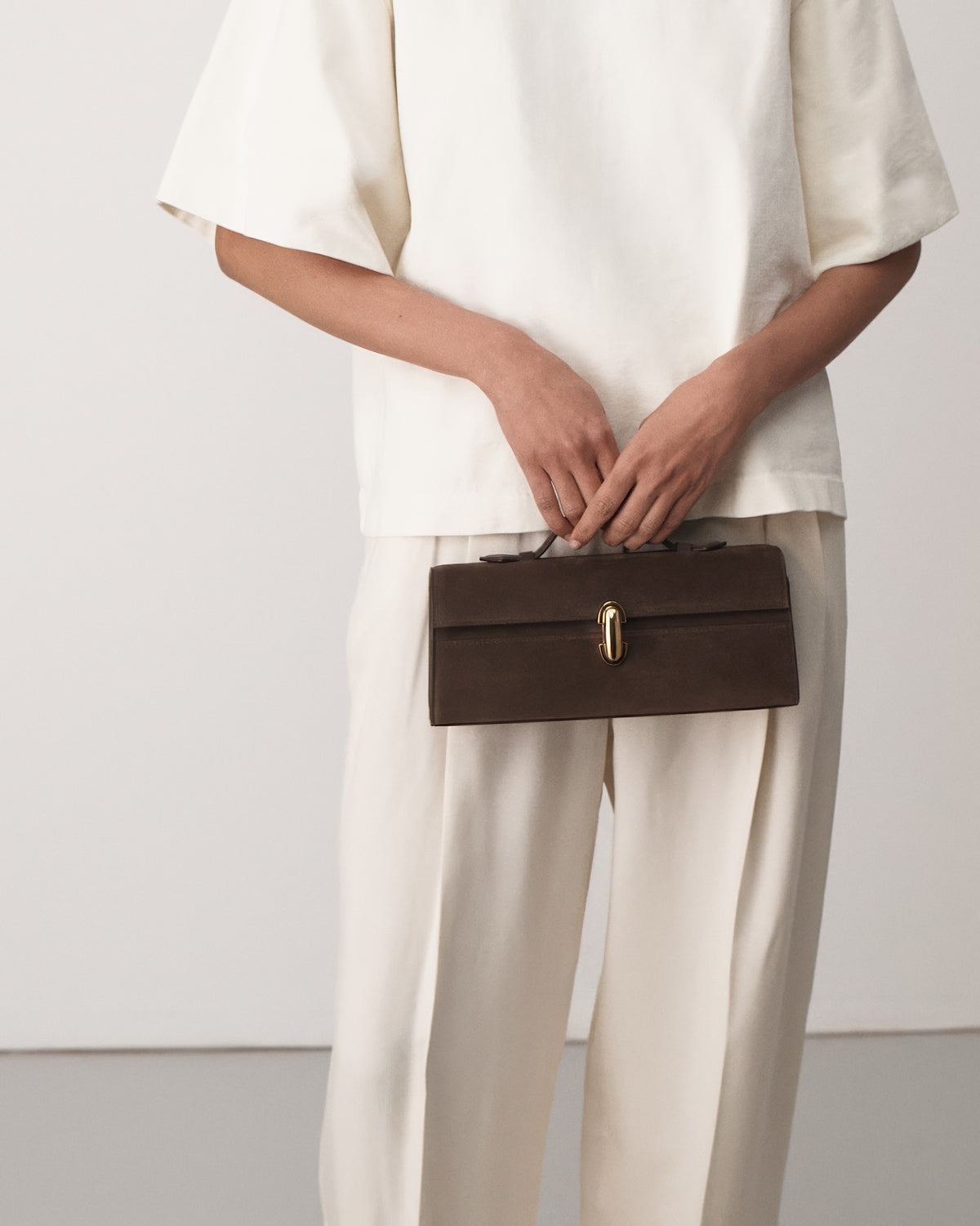 on-model view of a coffee brown suede top handle bag with a gold clasp on a white background 