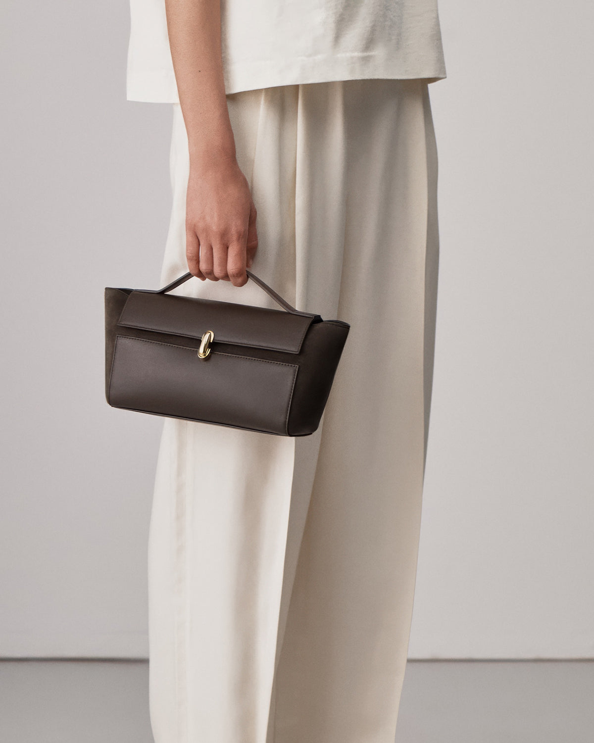 on-model view of a coffee brown leather shoulder bag with a leather covered gold clasp on a white background 