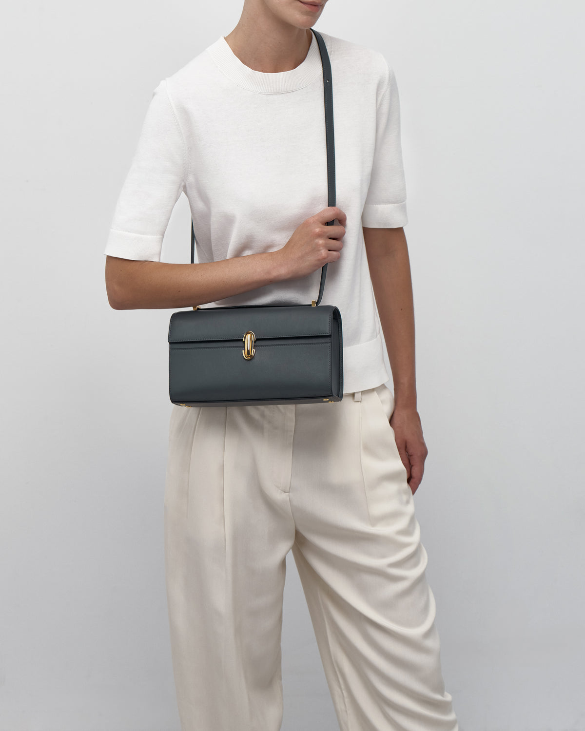 on model view of a storm blue leather bag with a gold clasp on a white background