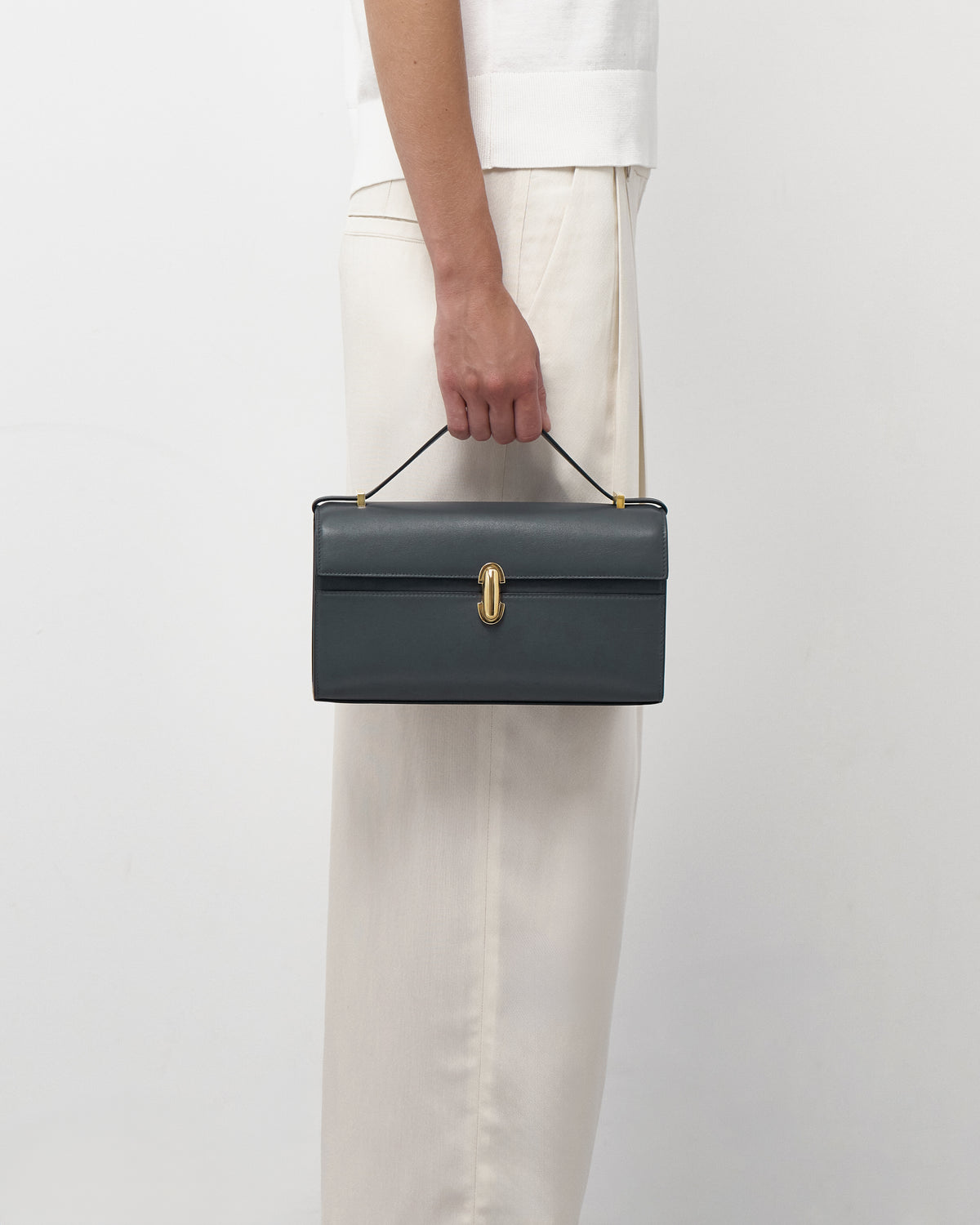 on model view of a storm blue leather bag with a gold clasp on a white background