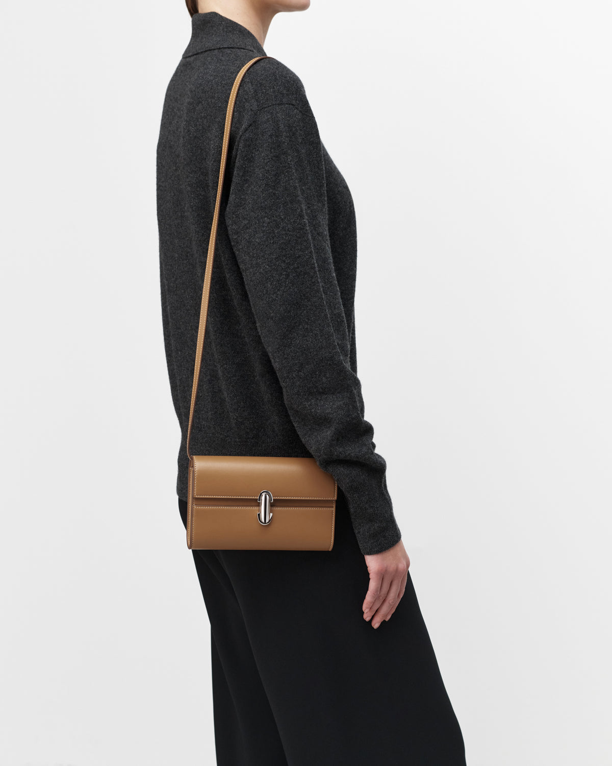 On model view of saddle leather handbag with silver hardware and a crossbody strap on a white background