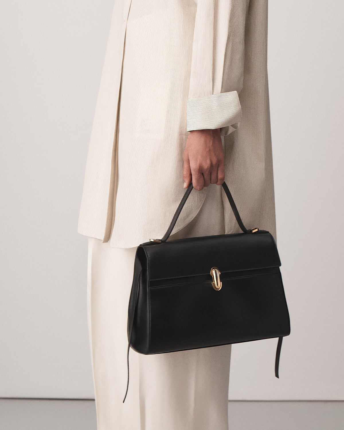 on-model view of a black leather handbag with gold clasp on a white background 