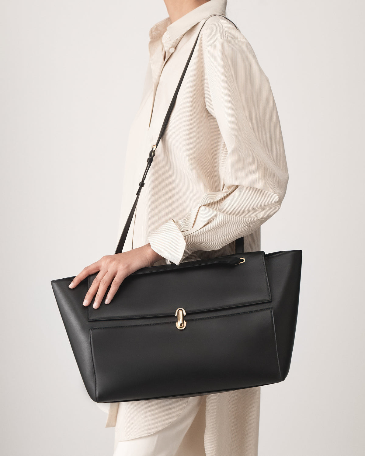 on-model view of a black leather tote bag with a gold clasp on a white background 