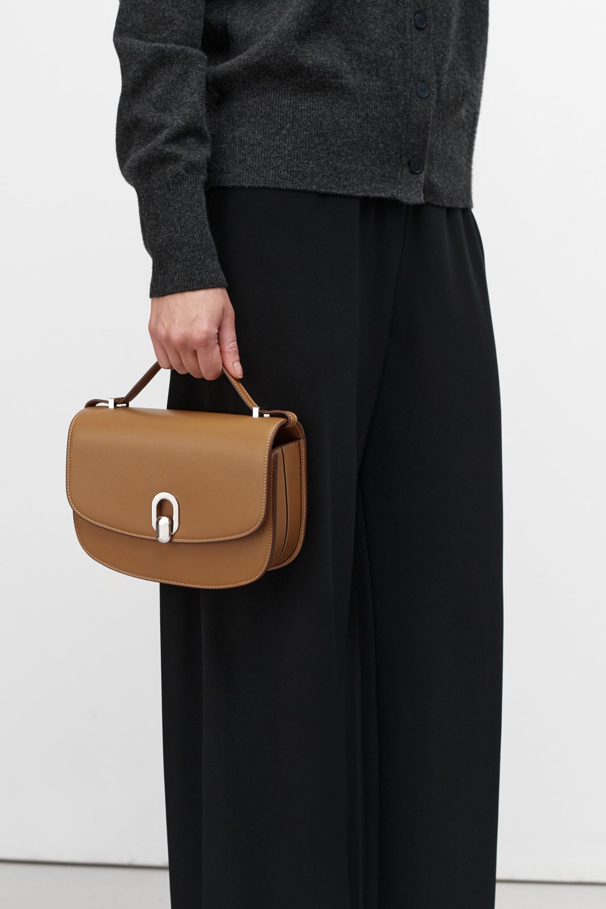 On model view of saddle leather handbag with silver hardware and a crossbody strap on a white background