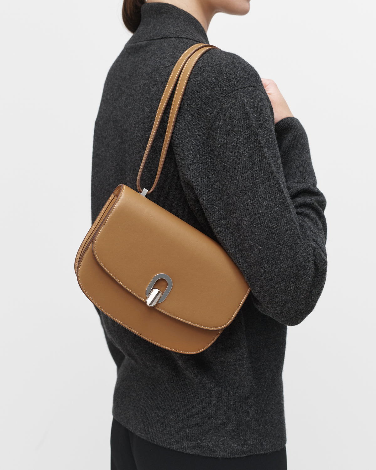 On model view of saddle leather handbag with silver hardware and a crossbody strap on a white background