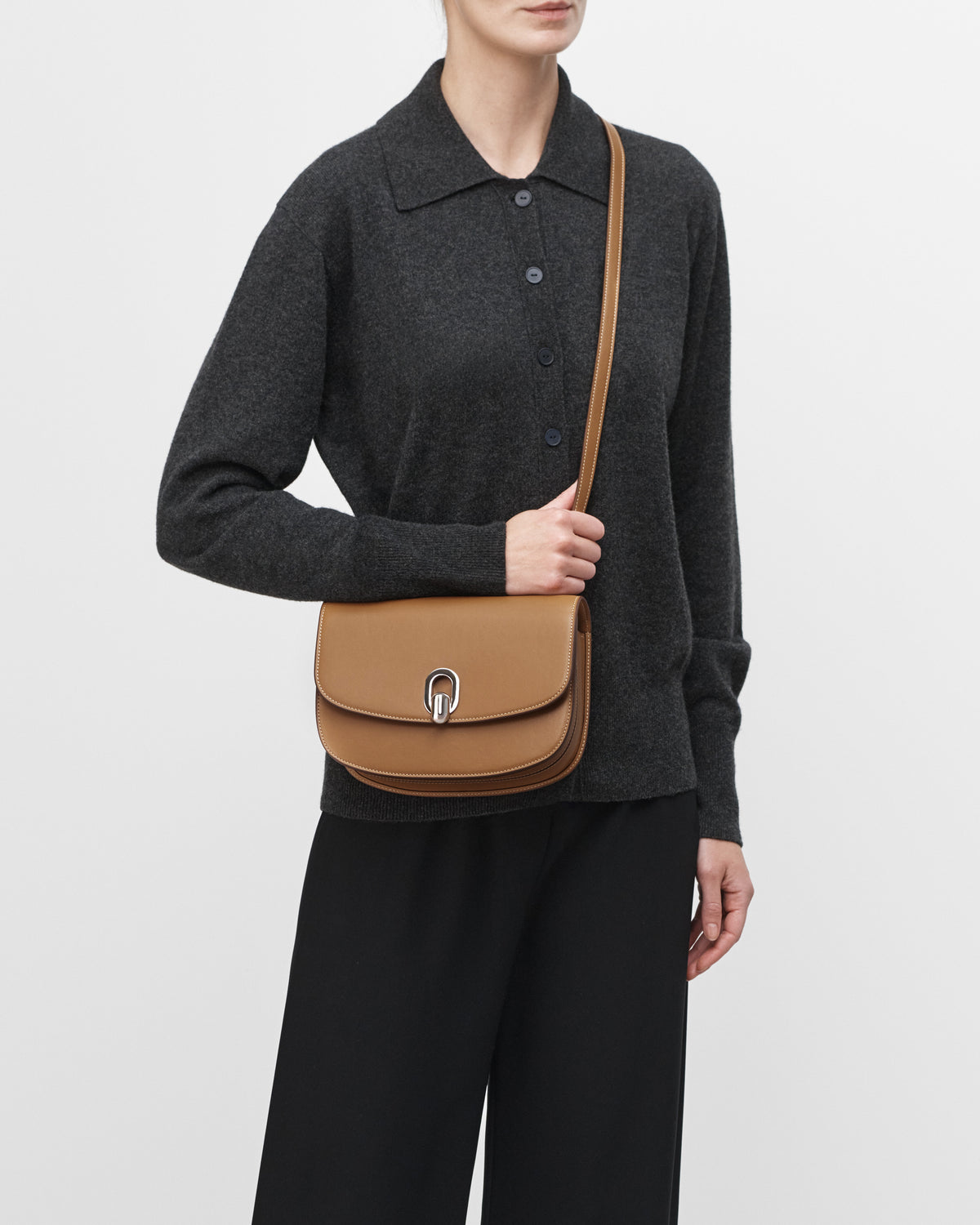 On model view of saddle leather handbag with silver hardware and a crossbody strap on a white background