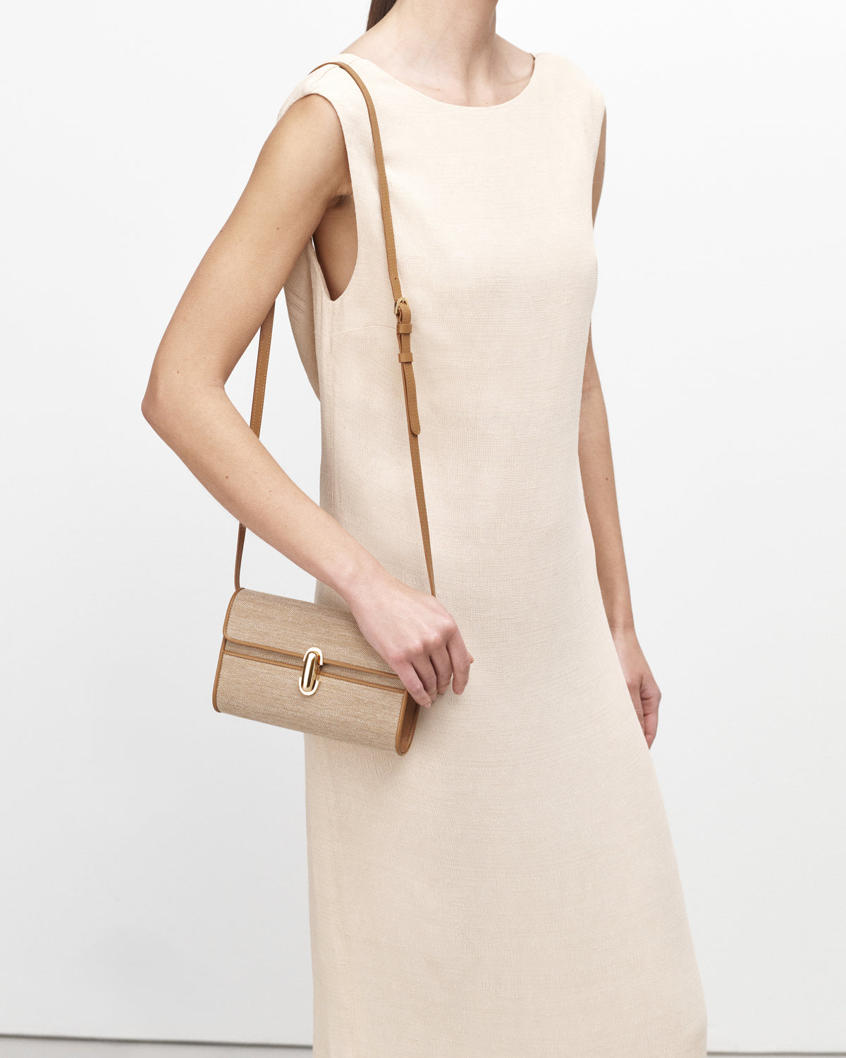 On model view of beige handbag with a brown strap and gold hardware on a white background