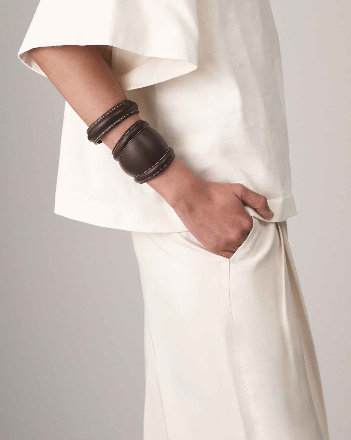 on model view of a coffee brown leather cuff with white stitching on a white background