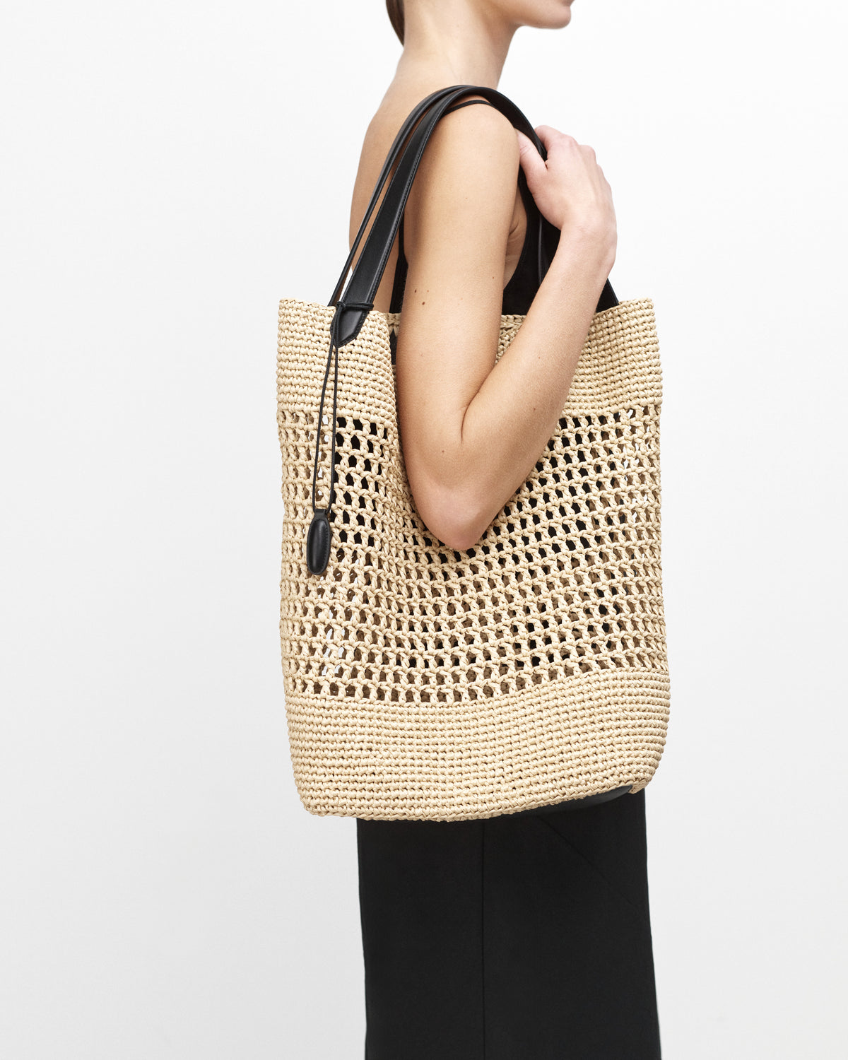 On model view raffia tote bag with black handle on a white background