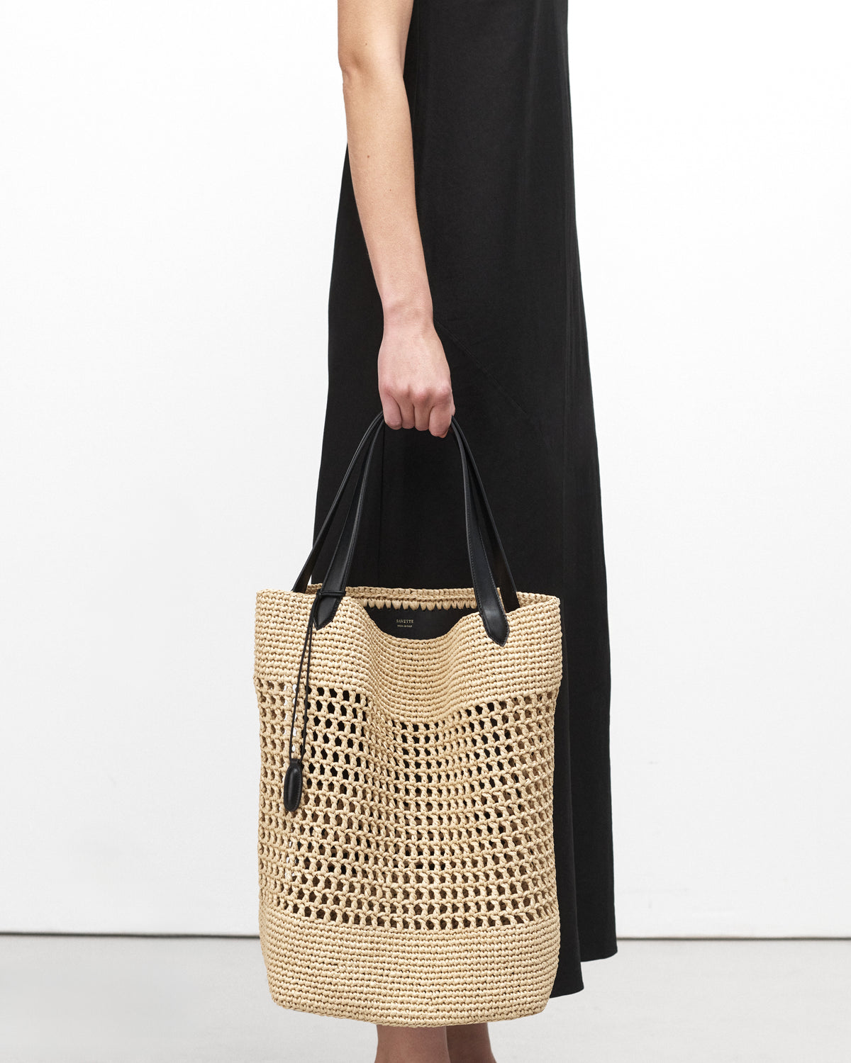 On model view raffia tote bag with black handle on a white background