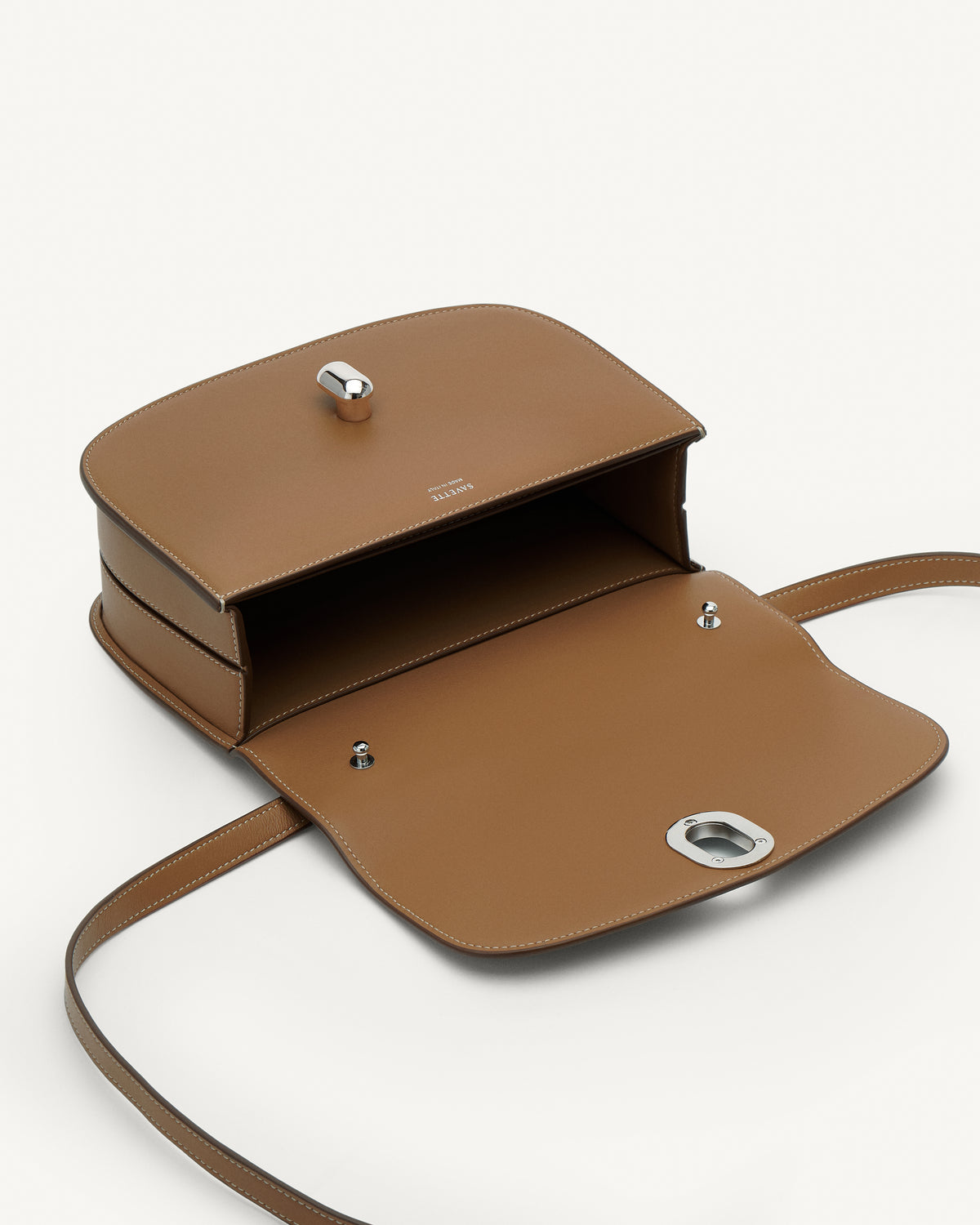 Inside view of saddle leather handbag with silver hardware and a crossbody strap on a white background