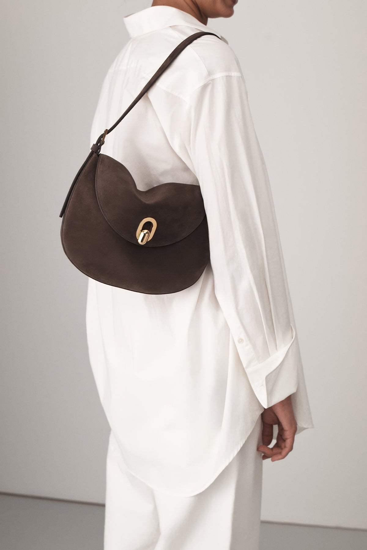on model view of a coffee brown suede shoulder bag with gold hardware on a white background