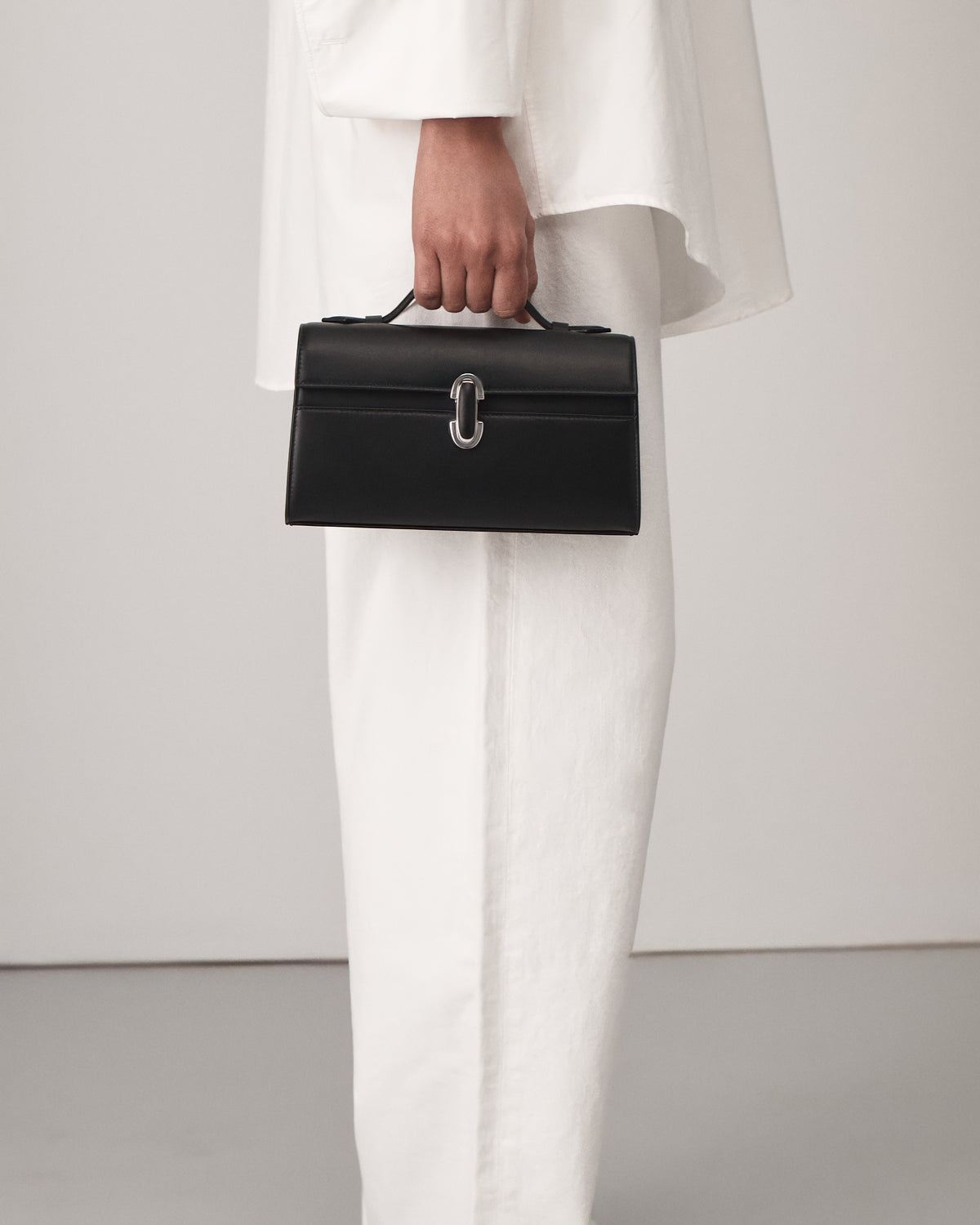 on model view of a black leather top handle bag with a black leather covered silver clasp on a white background
