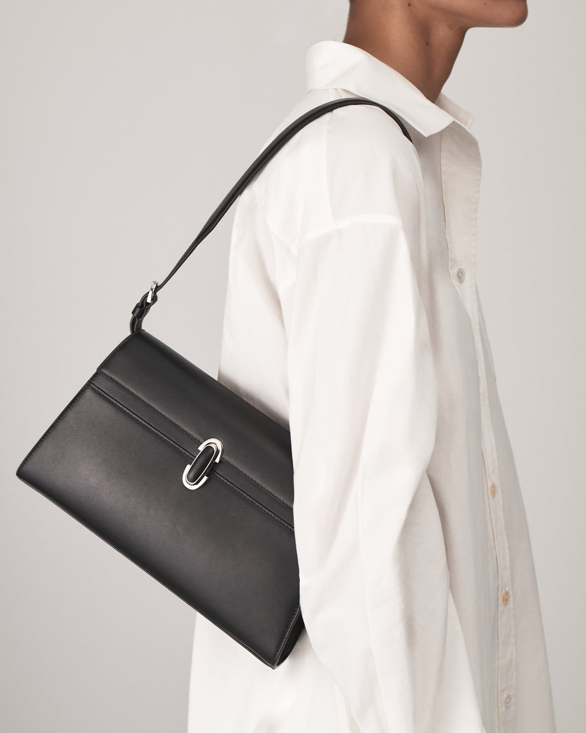 on model view of a black leather shoulder bag with a black leather covered silver clasp on a white background