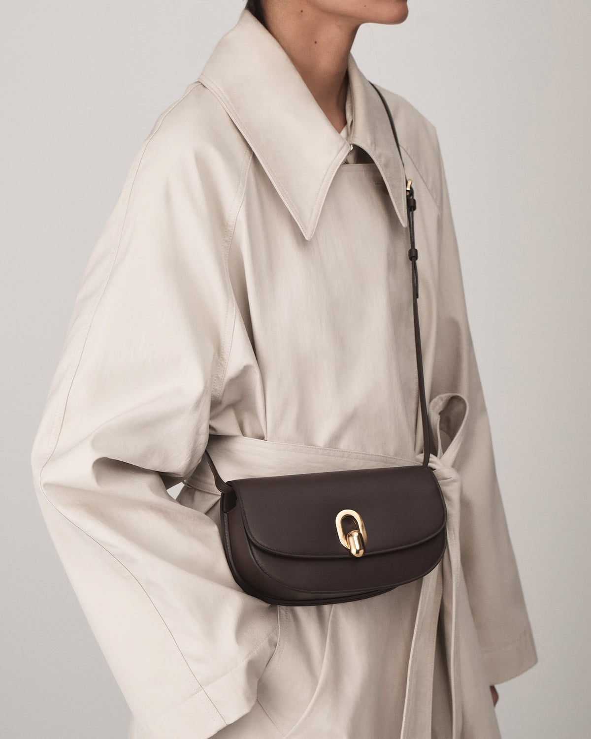 on model view of a coffee brown leather handbag with gold hardware on a white background
