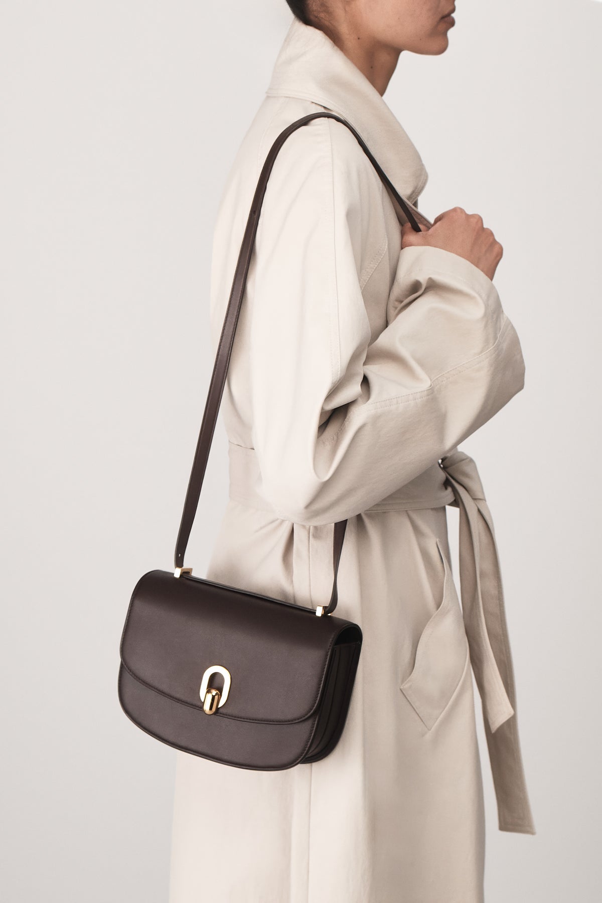 on model view of a coffee brown leather bag with gold hardware on a white background