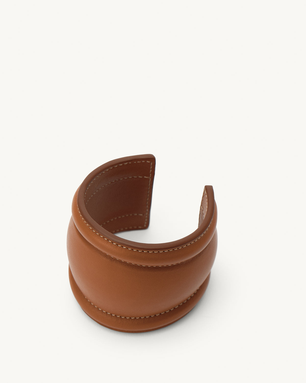 front aerial view of a cognac brown leather cuff with white stitching on a white background 