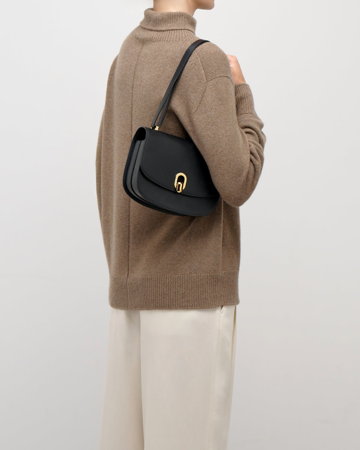 on model image of a black leather bag with gold hardware on a white background
