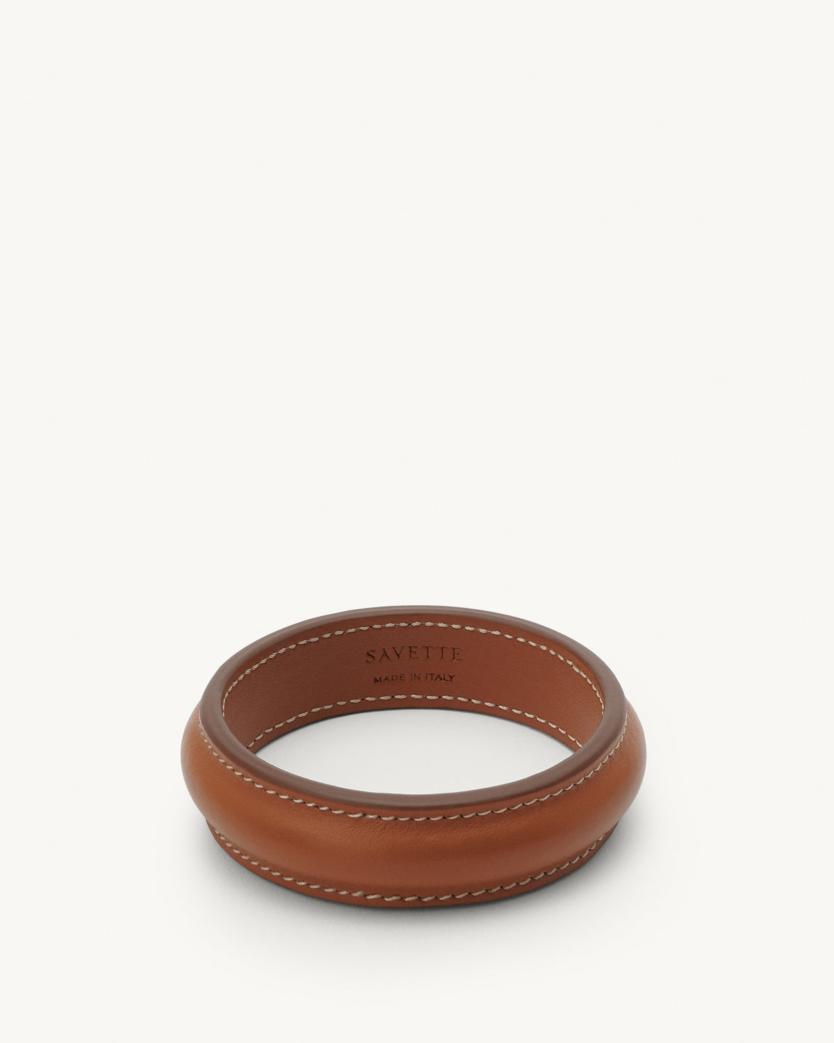 front view of a cognac brown leather bangle with white stitching on a white background