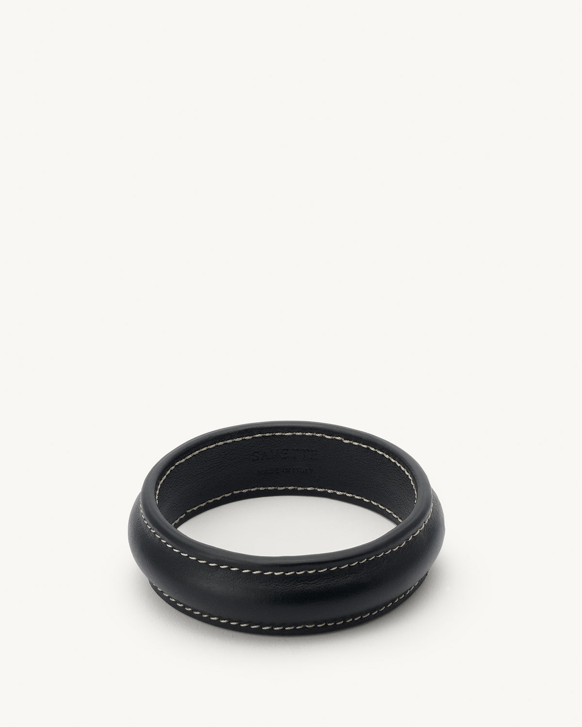 front view of a black leather bangle with white stitching on a white background