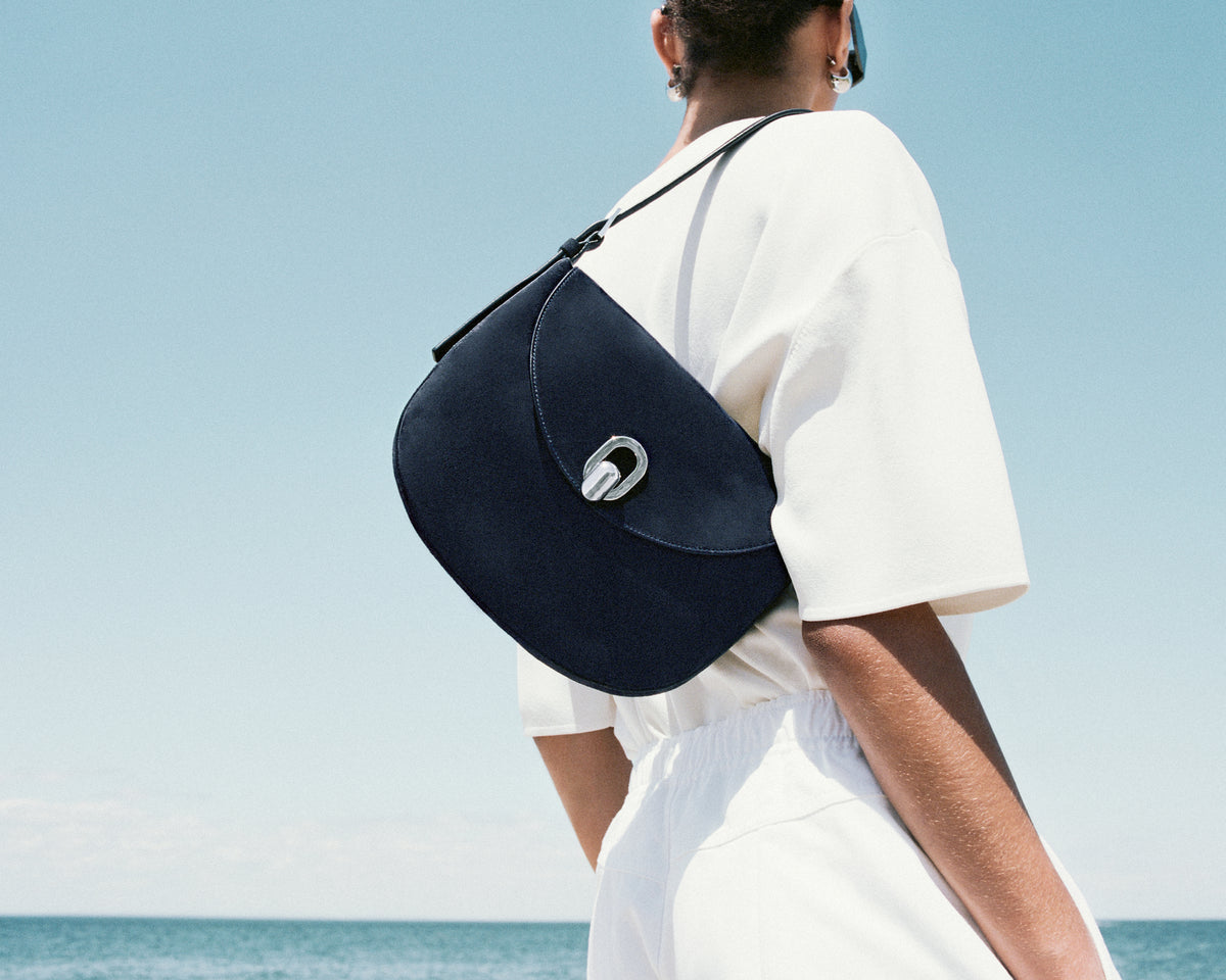 on model image of navy blue bag with silver clasp in outdoor background