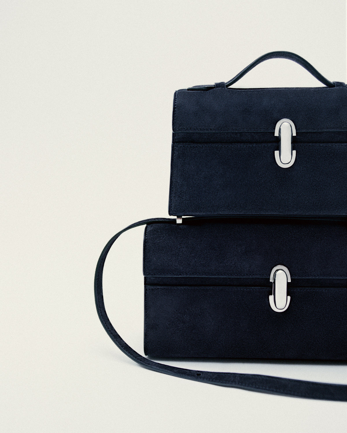 front view of two navy blue bags with silver clasps stacked on a white background