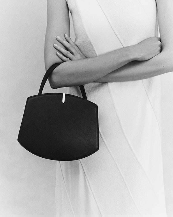 black and white front view of model holding black bag on a white background