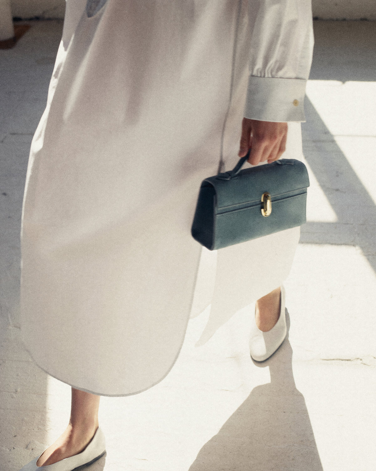 campaign on model image of blue suede bag with gold clasp in an outdoor background