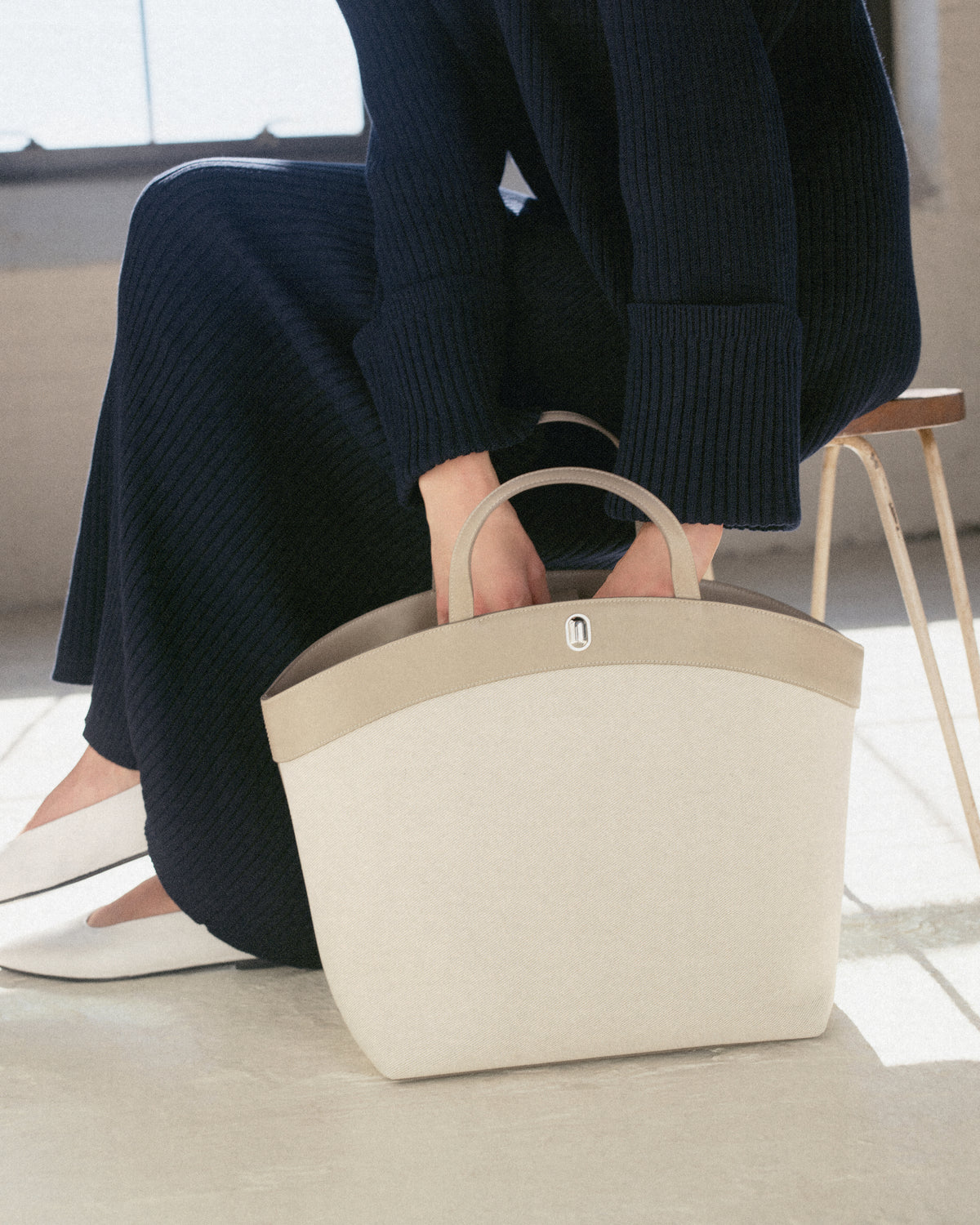 campaign image of beige canvas tote with leather trip with silver hardware