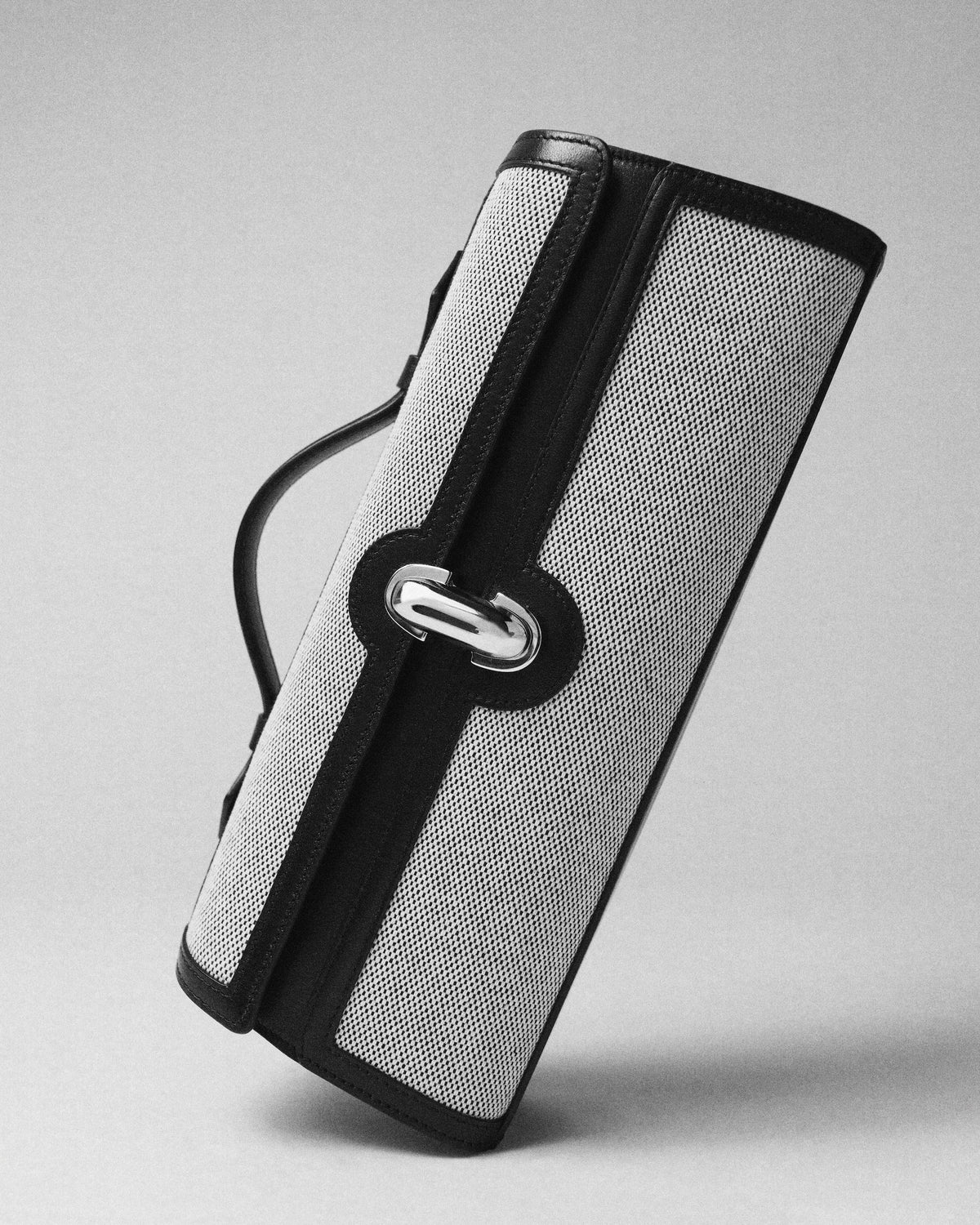 campaign image of grey canvas bag with black leather trim with silver clasp on a grey background