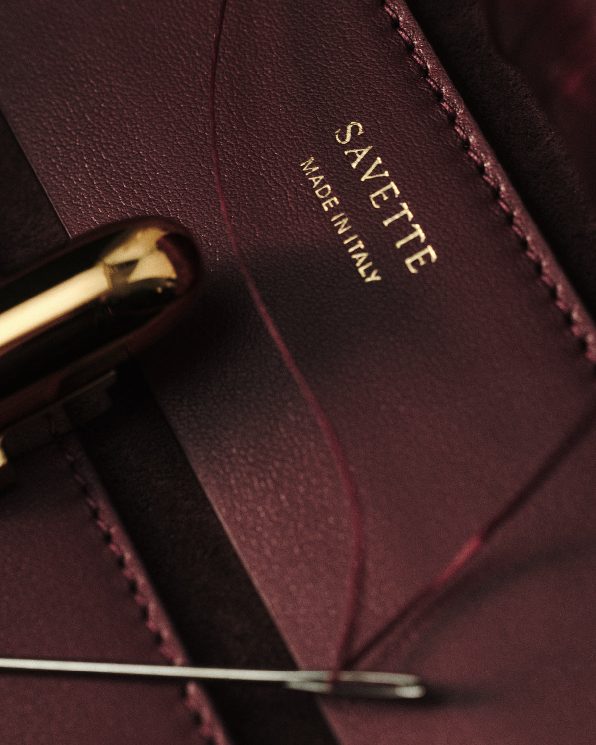campaign close up image of stitching wine red bag with gold hardware