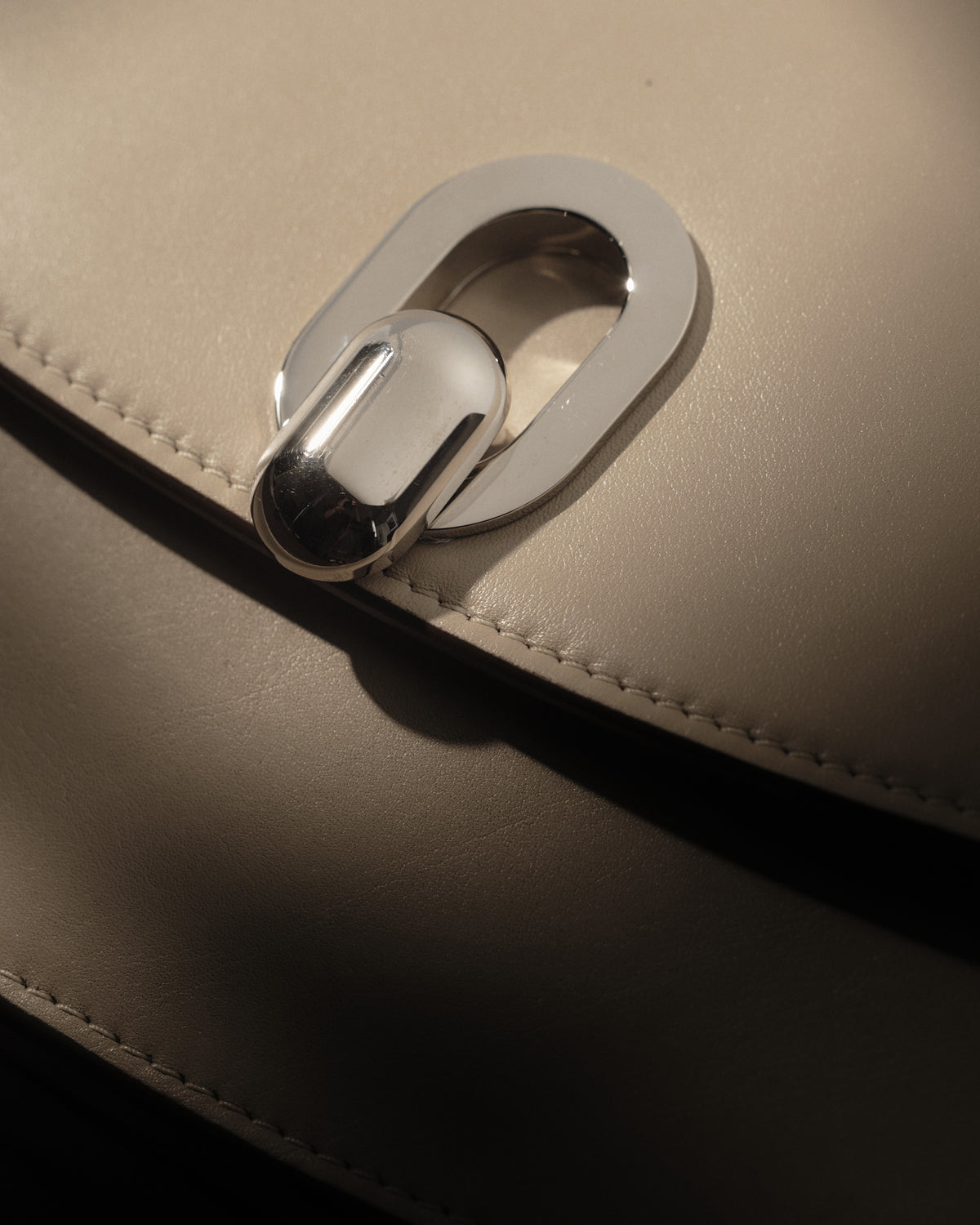 campaign close up image of bone beige leather bag with silver clasp on a black background