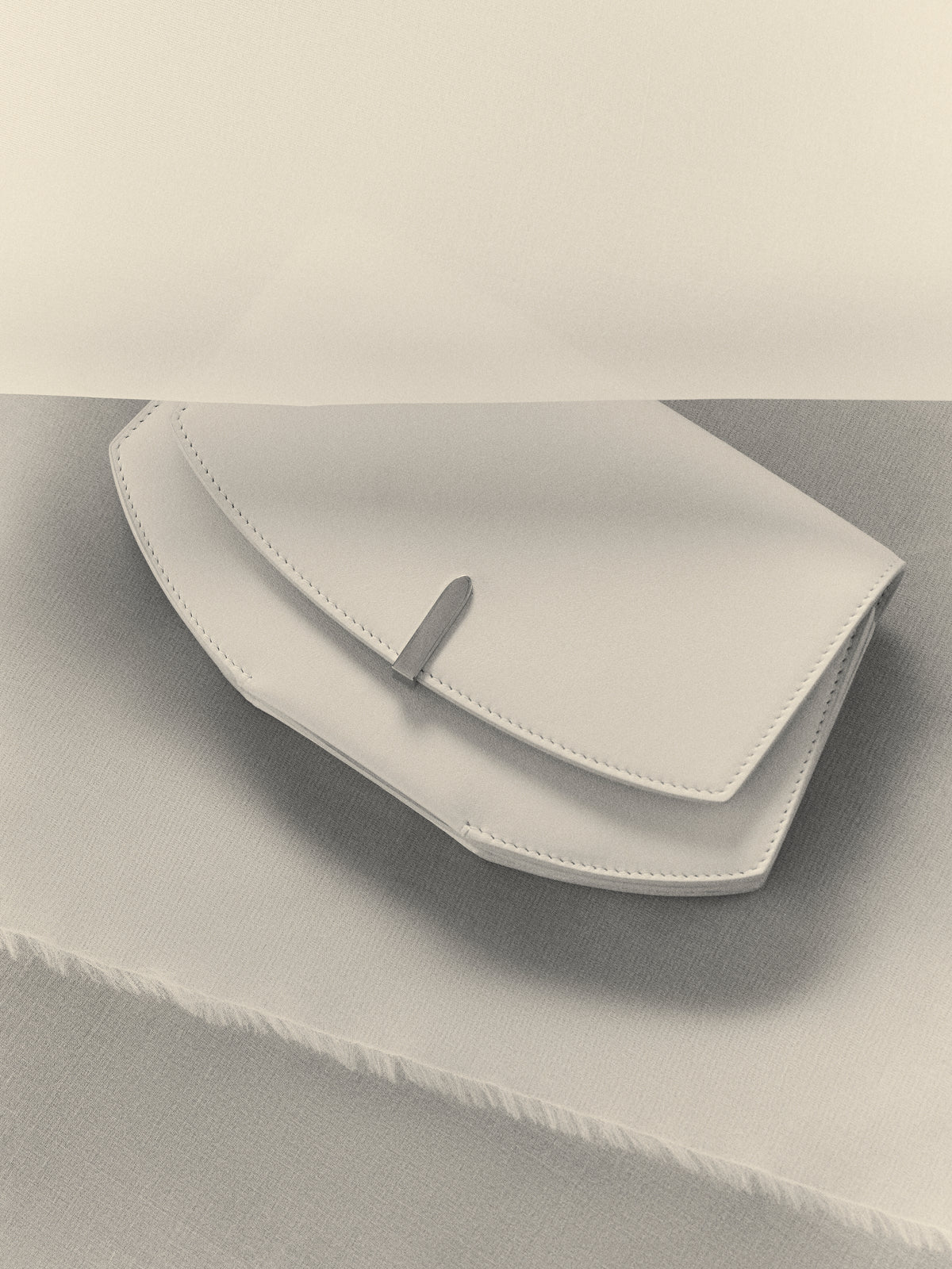 campaign image of a white leather clutch with silver hardware on a white background