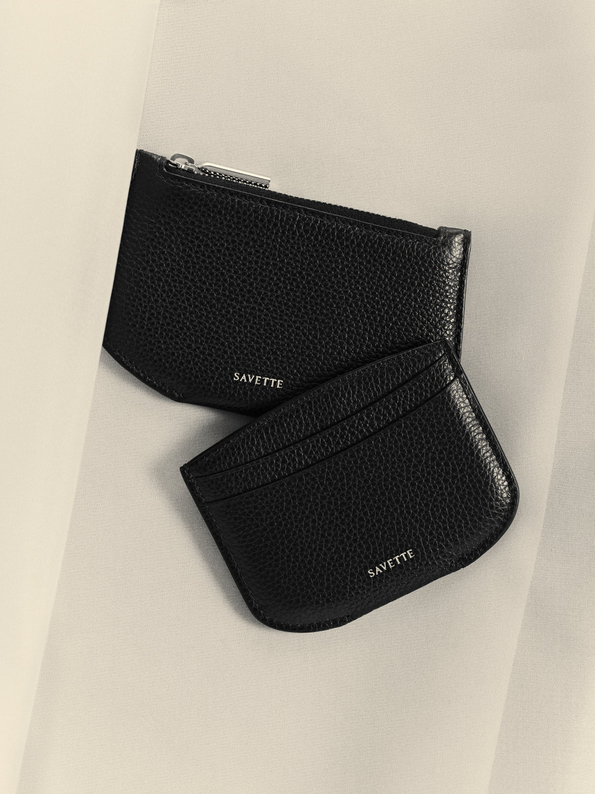 campaign aerial view of black card holder and black zipper wallet on an off white background