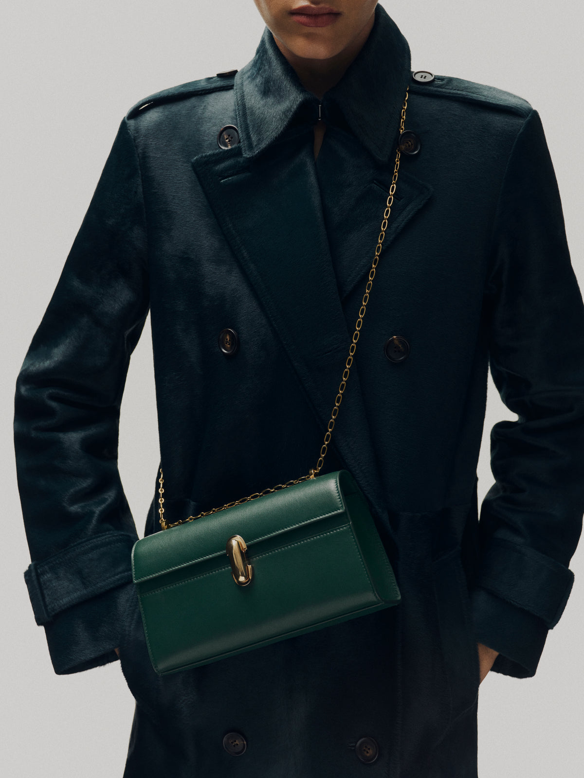 on model image of pine green bag with gold clasp and gold chain on an off white background