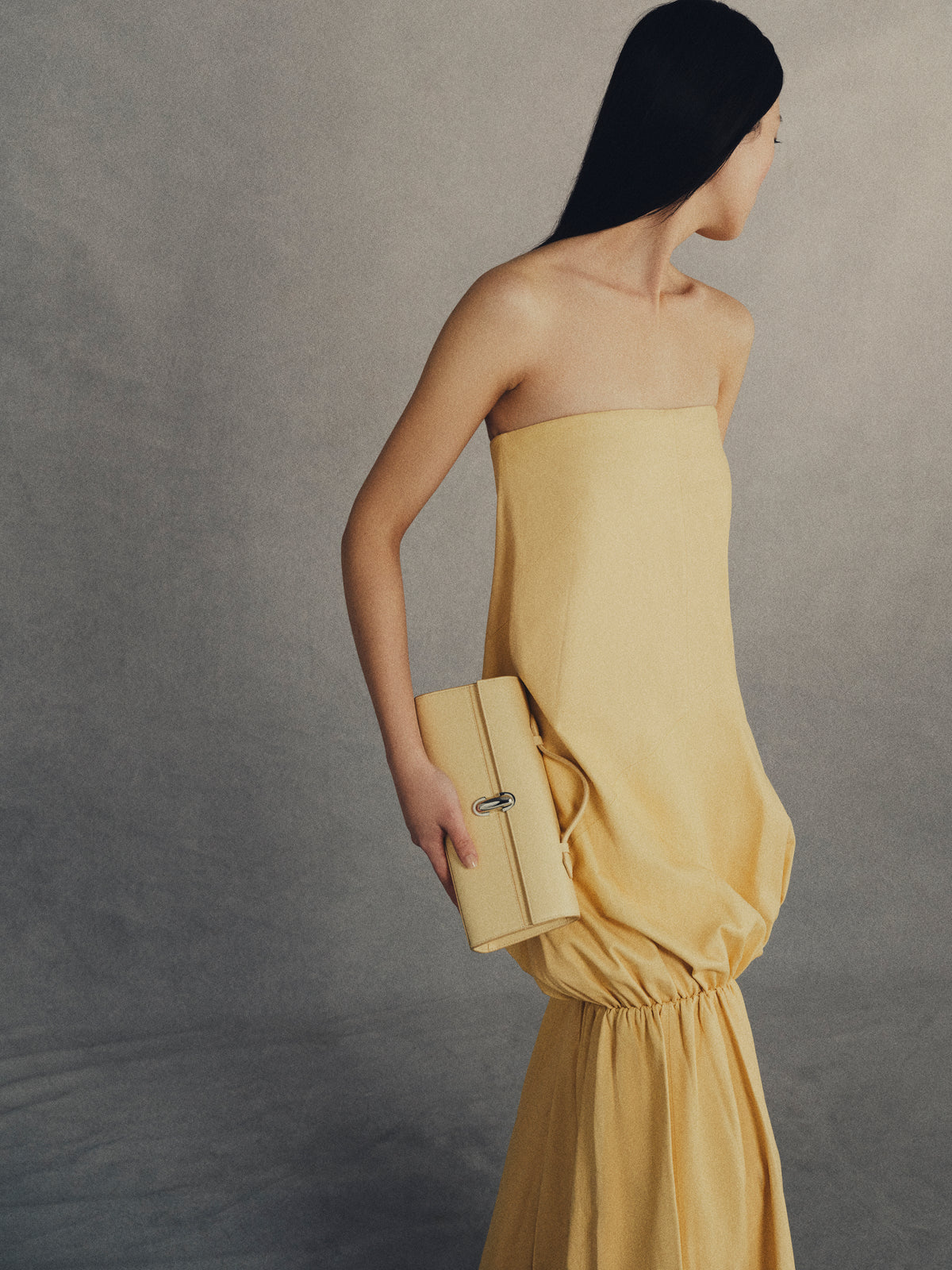 on model image of yellow bag with silver clasp on a grey background