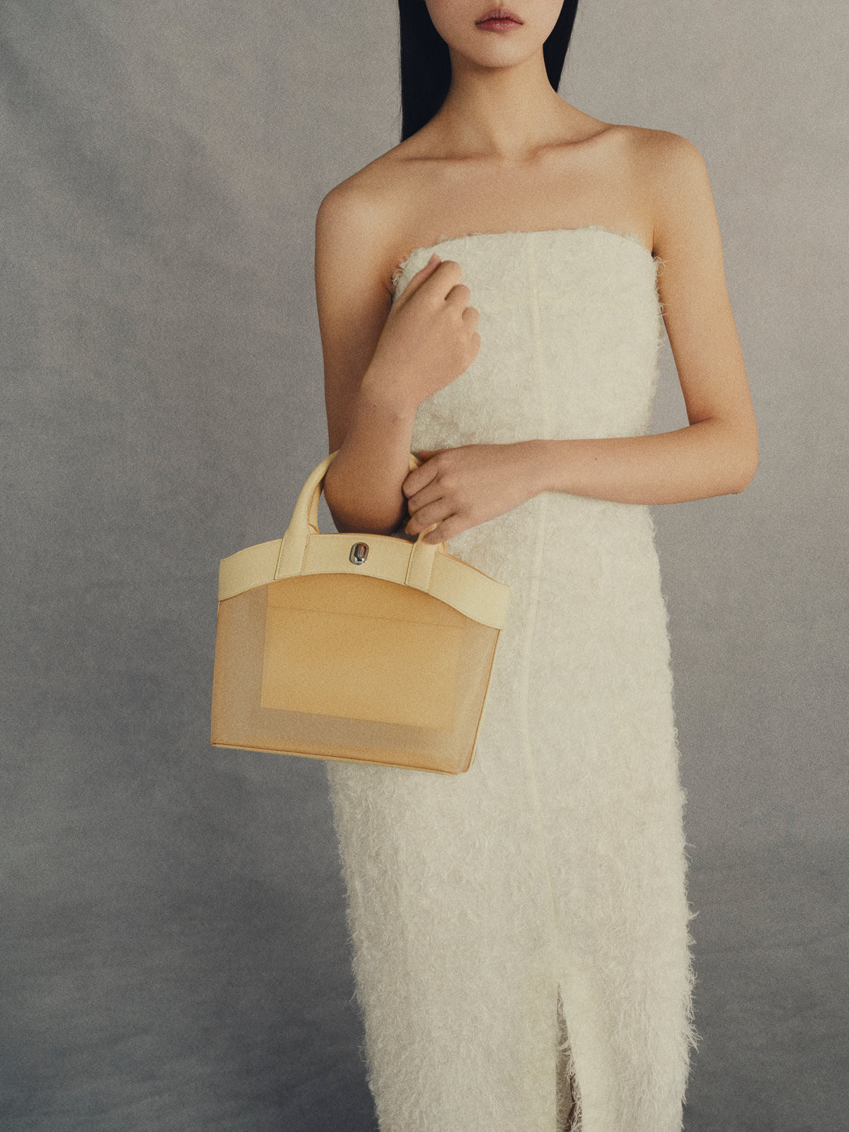 on model image of ecru mesh bag with leather trim and silver hardware on an a grey background